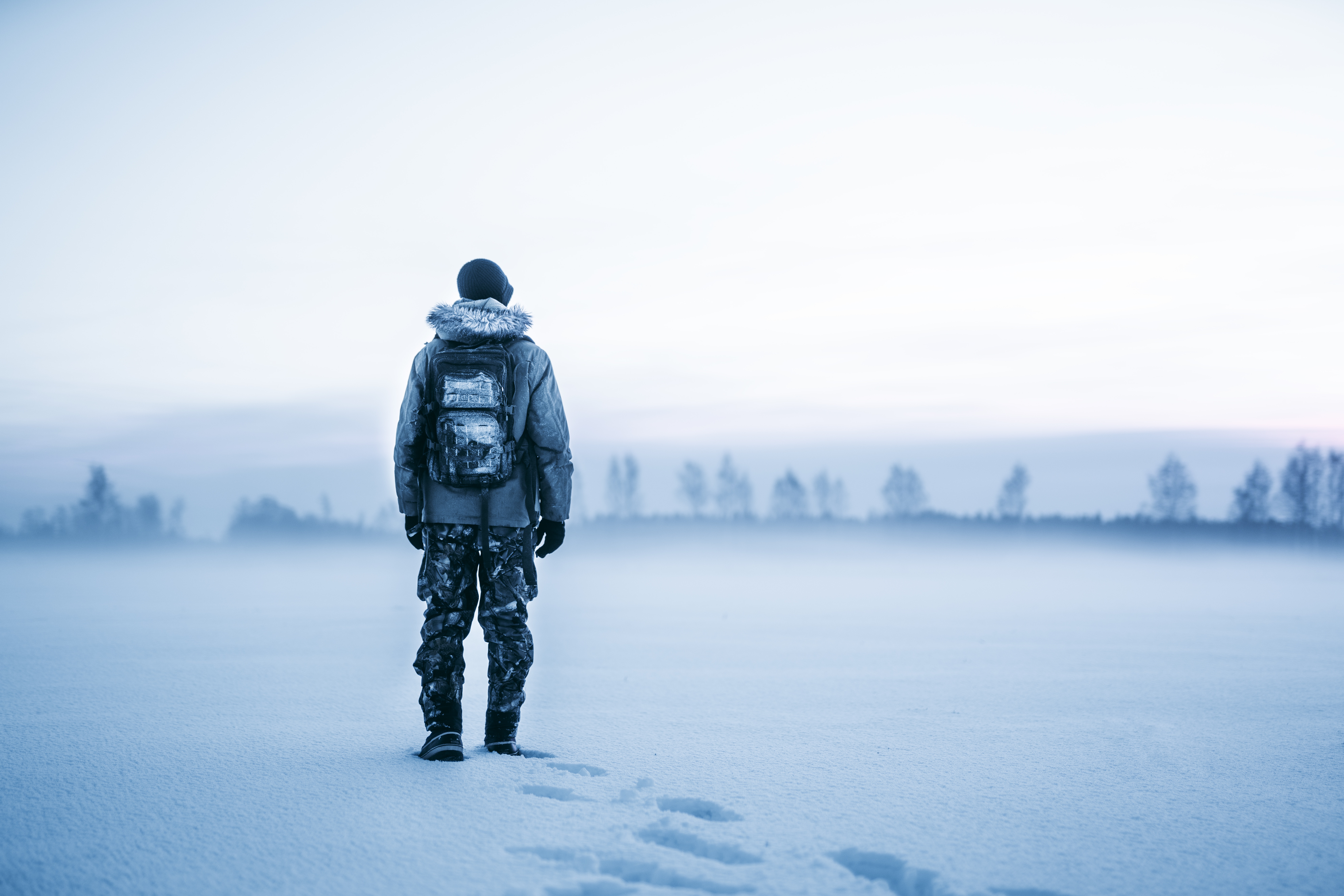 Man in winter coat with backpack in snowy landscape HD Wallpaper