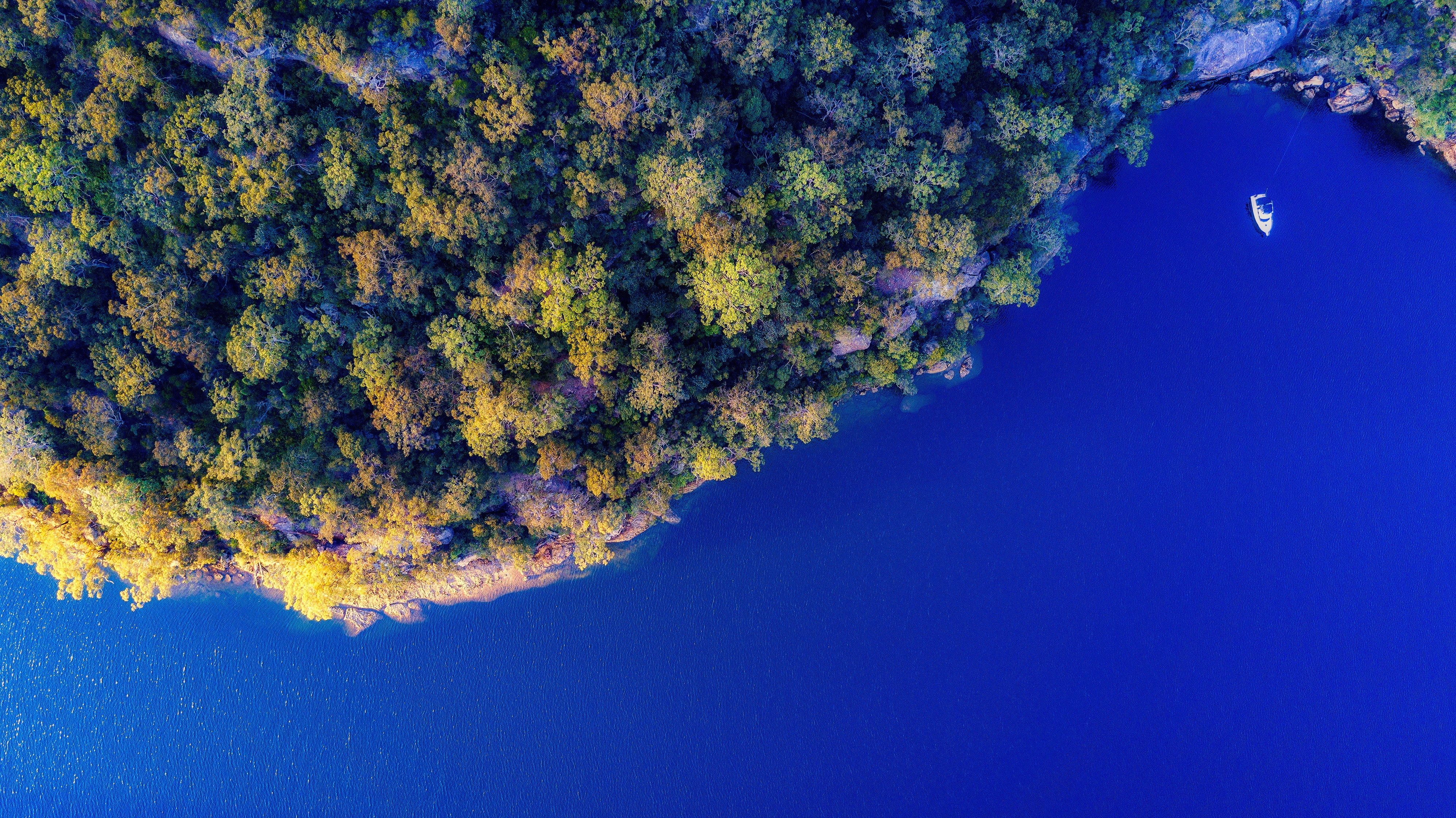 Aerial view of a forested island and blue water with a boat HD Wallpaper