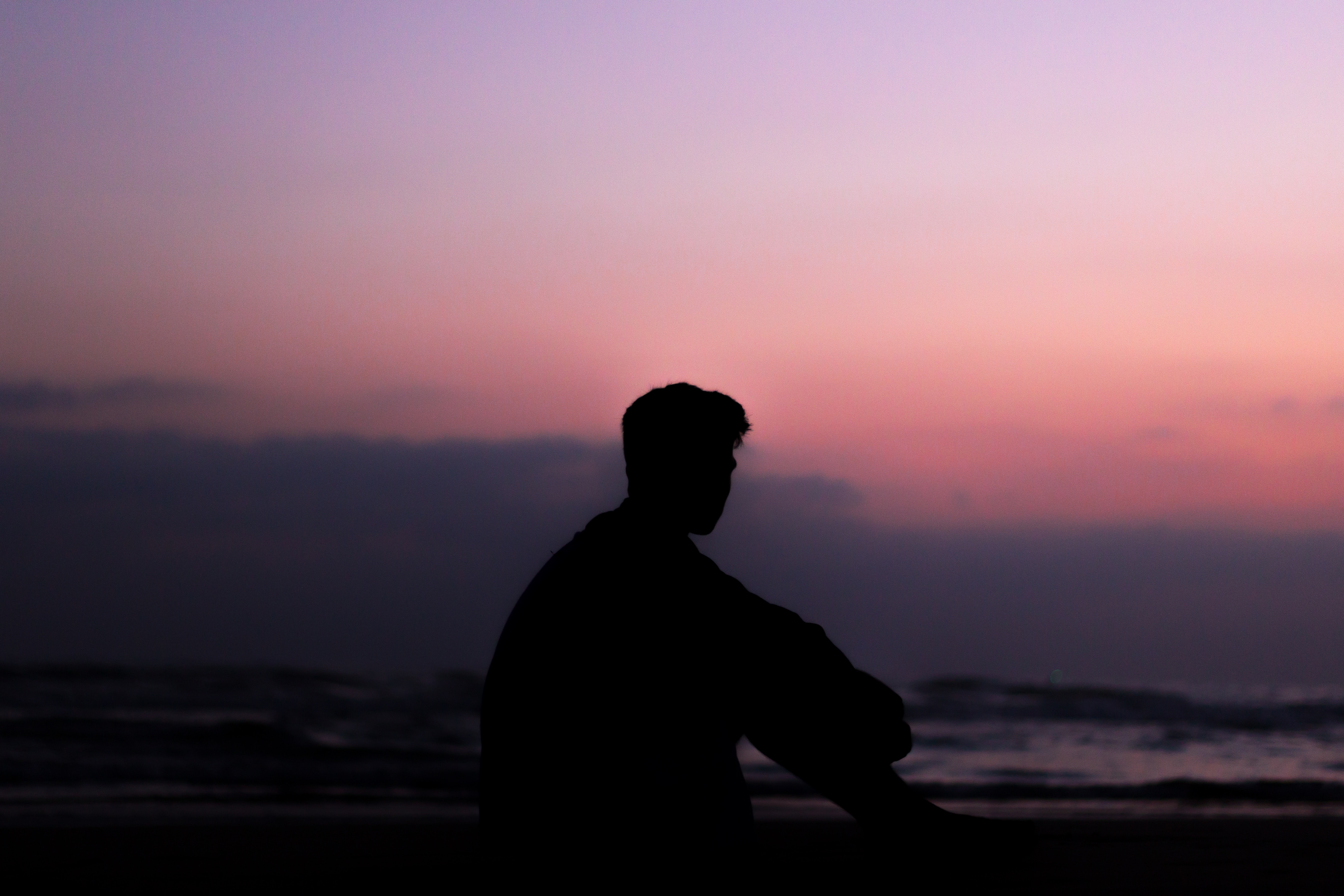 Silhouette of a man sitting on a beach at sunset HD Wallpaper