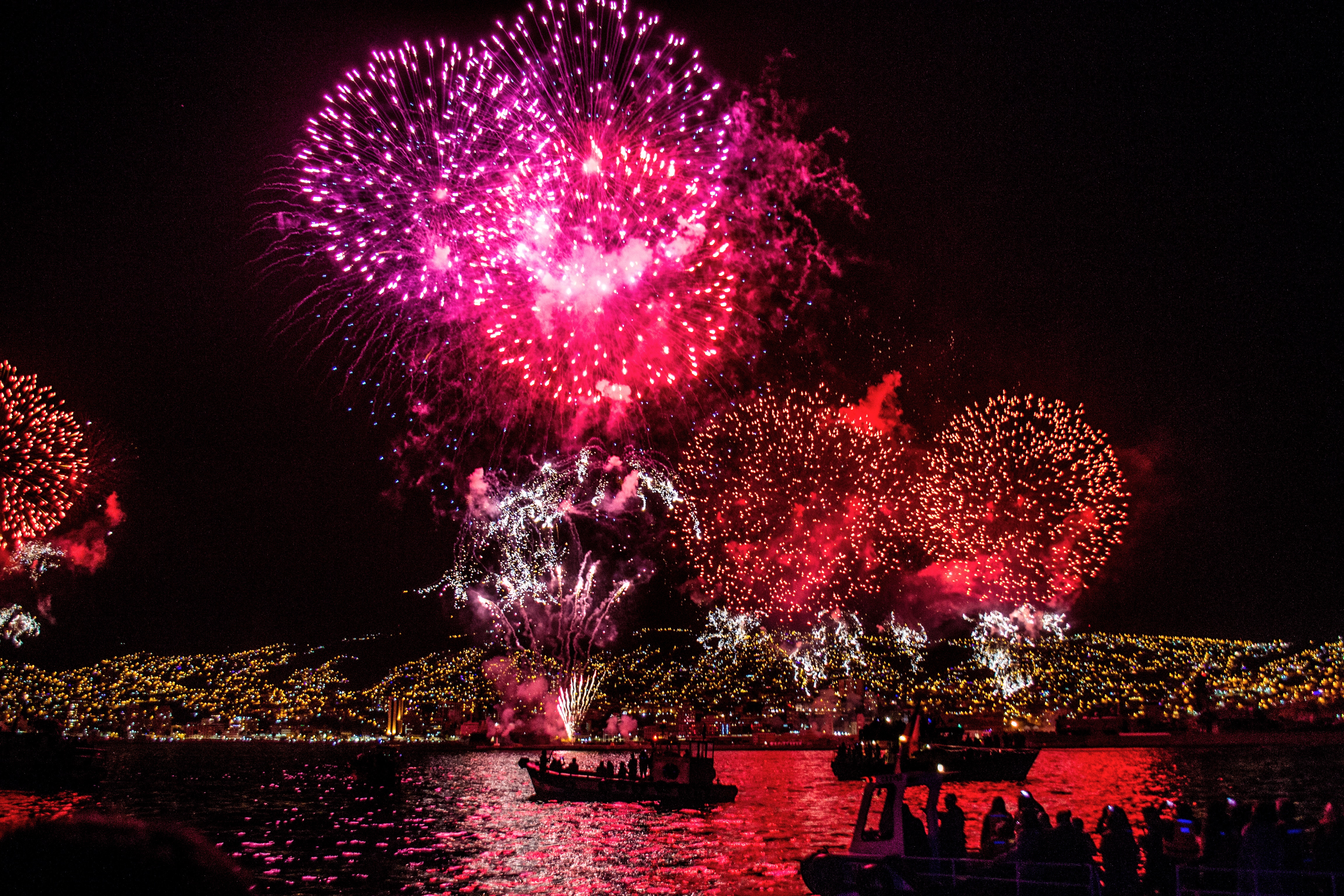 Fireworks over a city at night with boats on the water HD Wallpaper