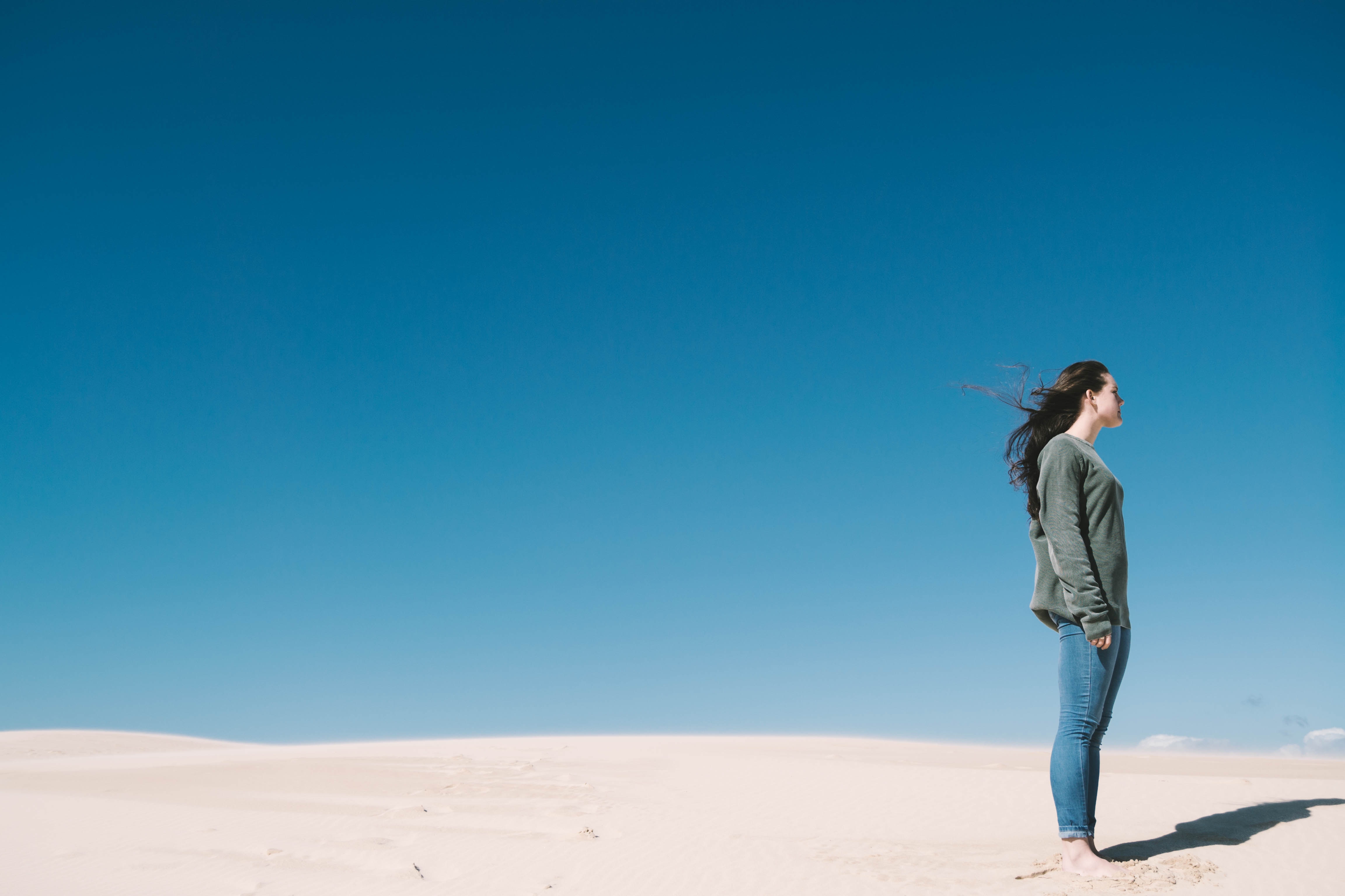 Woman standing on sand dunes under blue sky HD Wallpaper