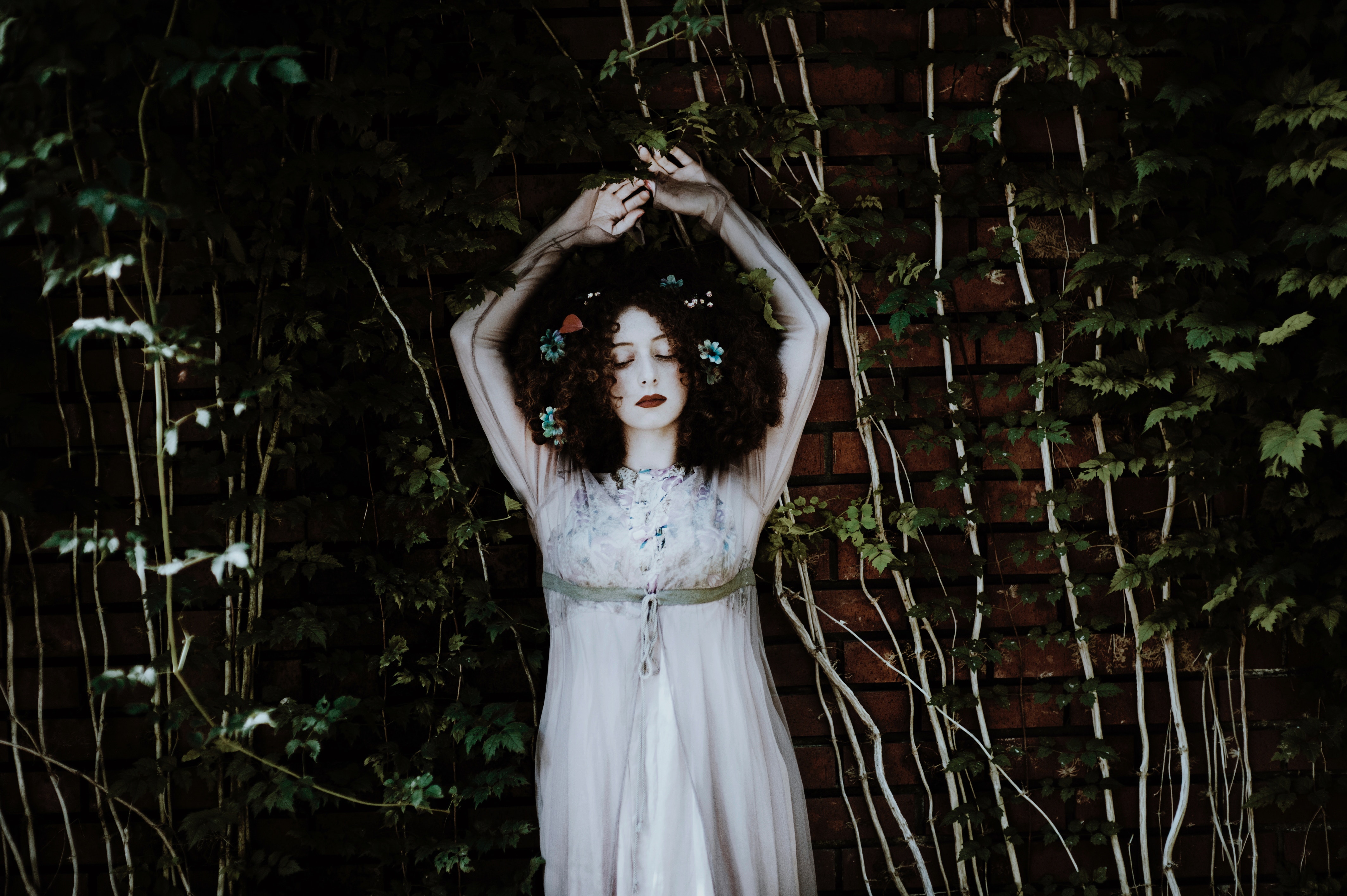 Woman with flowers in her hair in front of ivy wall HD Wallpaper