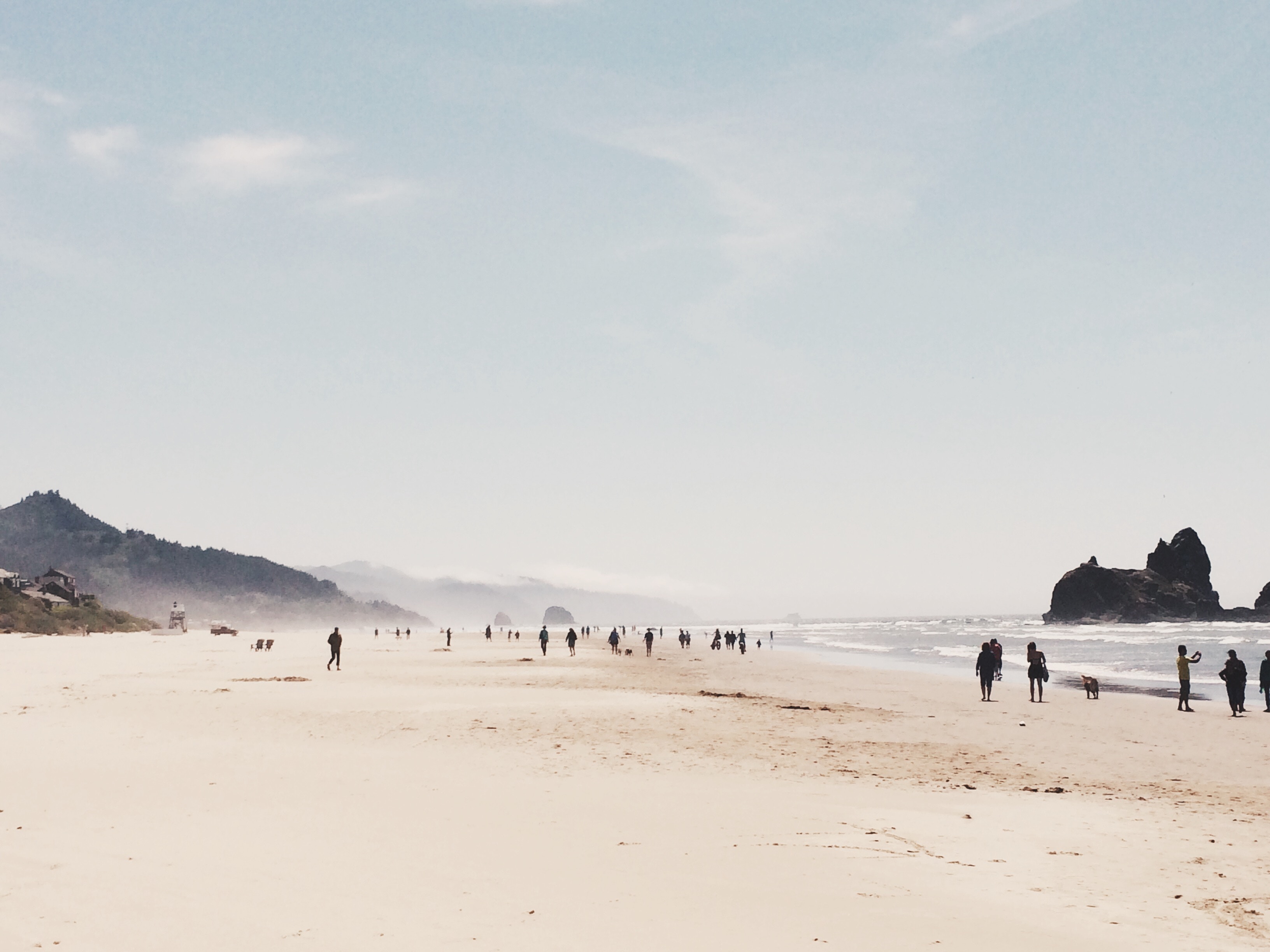 People walking on a sandy beach with rock formations HD Wallpaper
