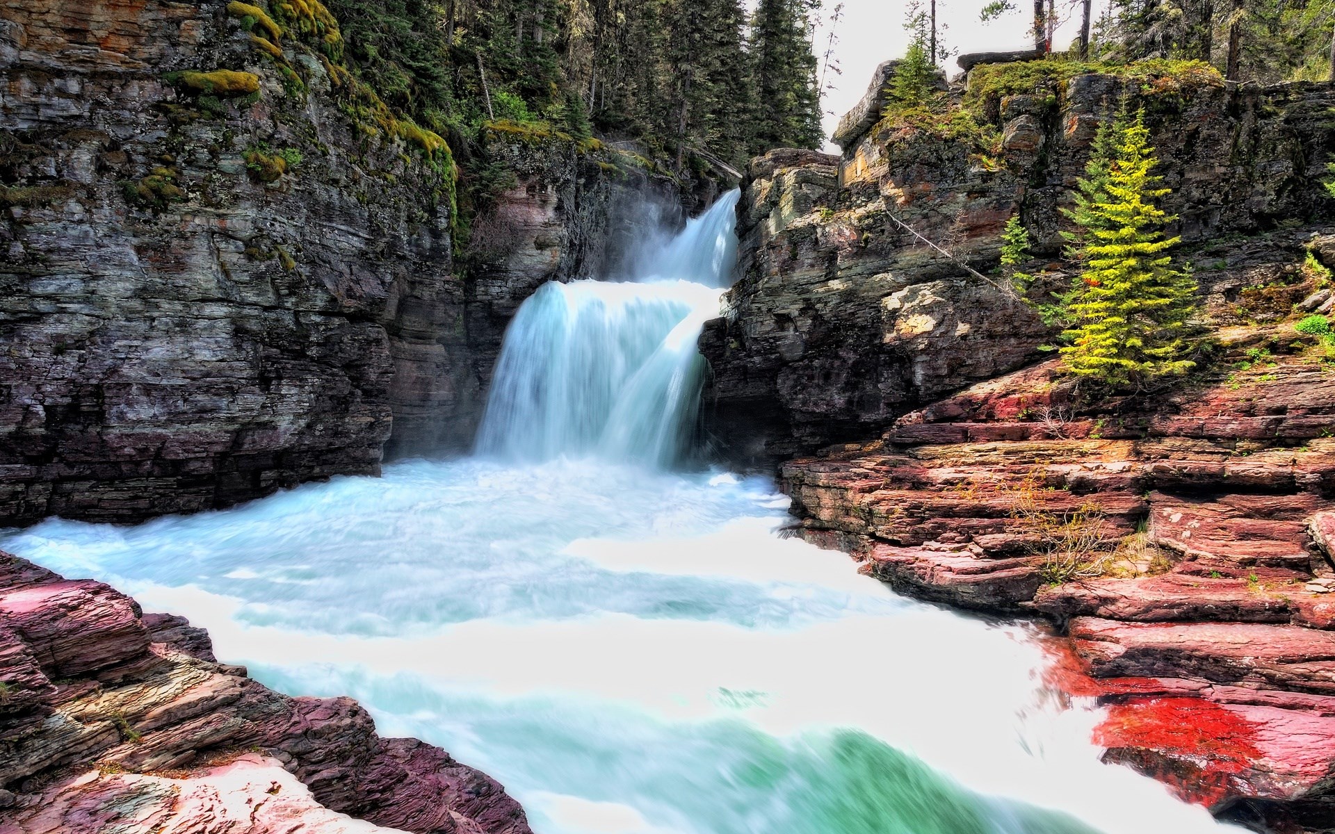 Waterfall cascading over red rocks in a forest HD Wallpaper