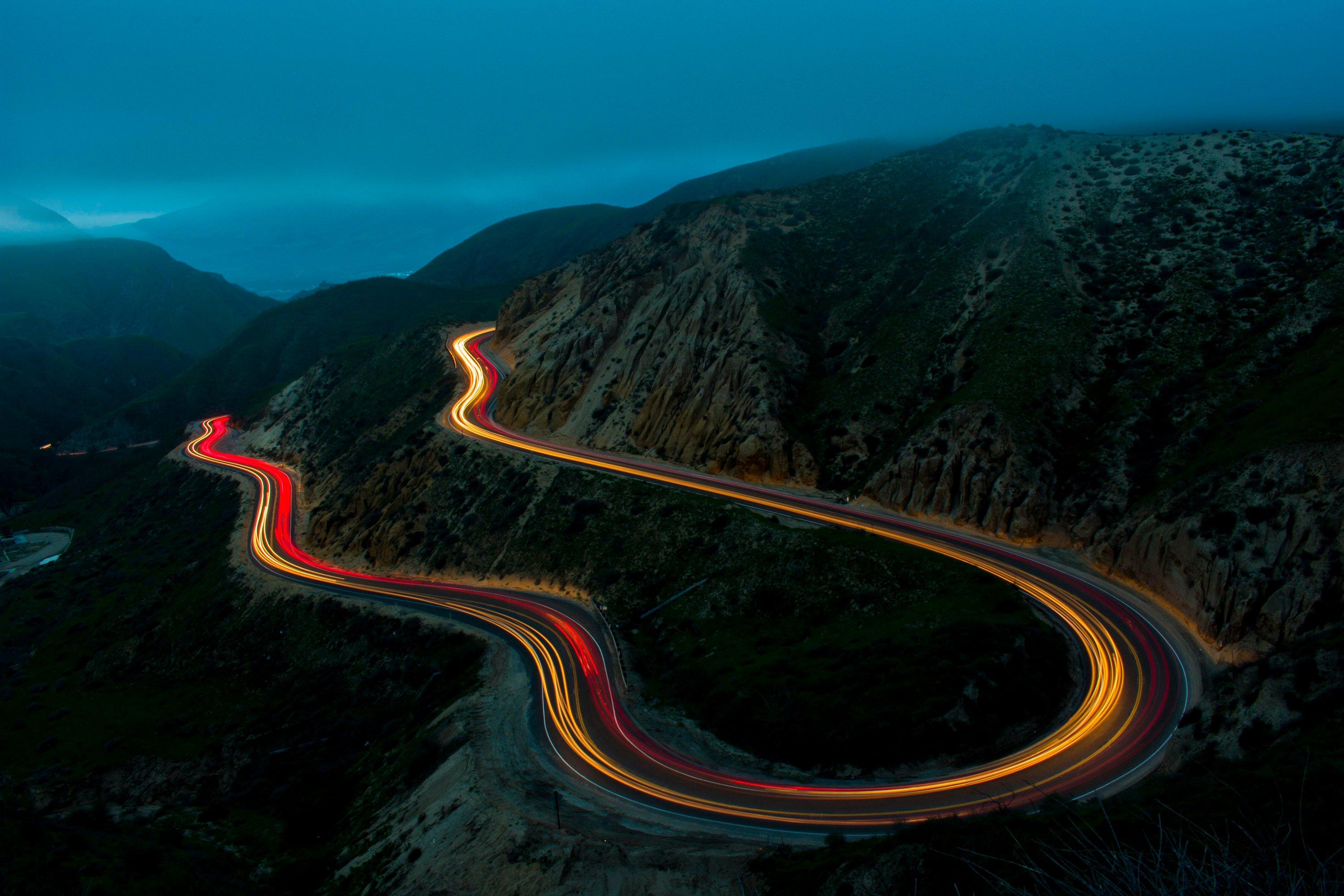 Time-lapse of car light trails on a winding mountain road at night HD Wallpaper