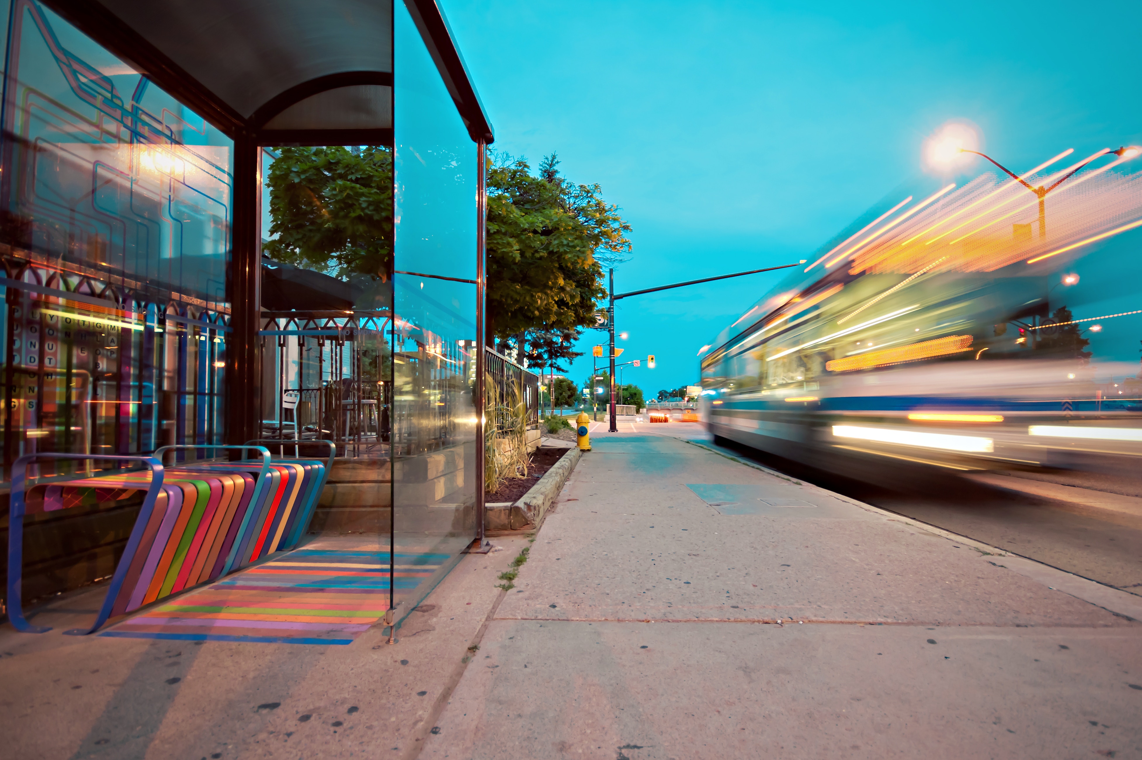 Bus stop with rainbow seat and blurred bus at dusk HD Wallpaper