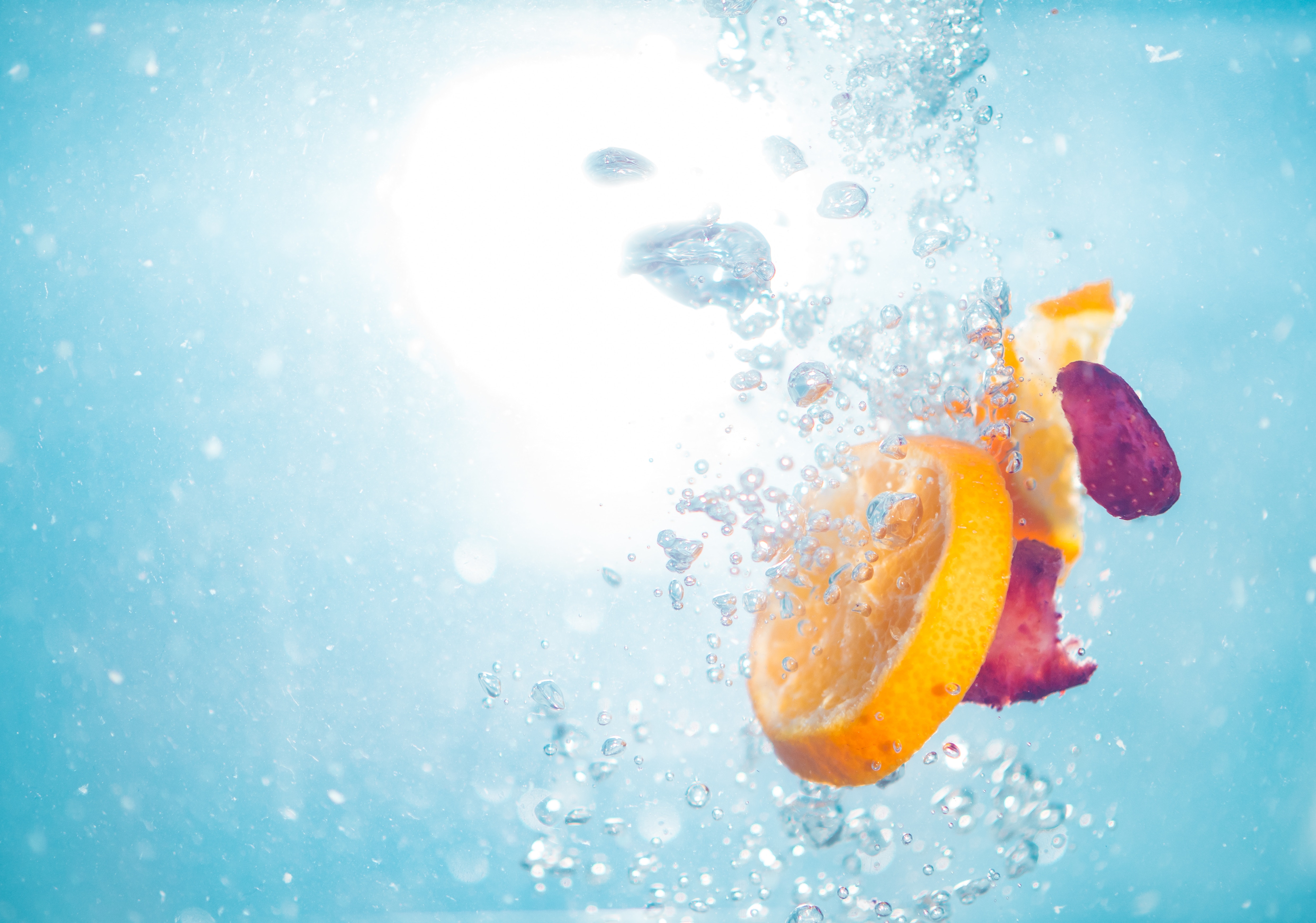 Orange slice and berries submerged in water with sunlight HD Wallpaper
