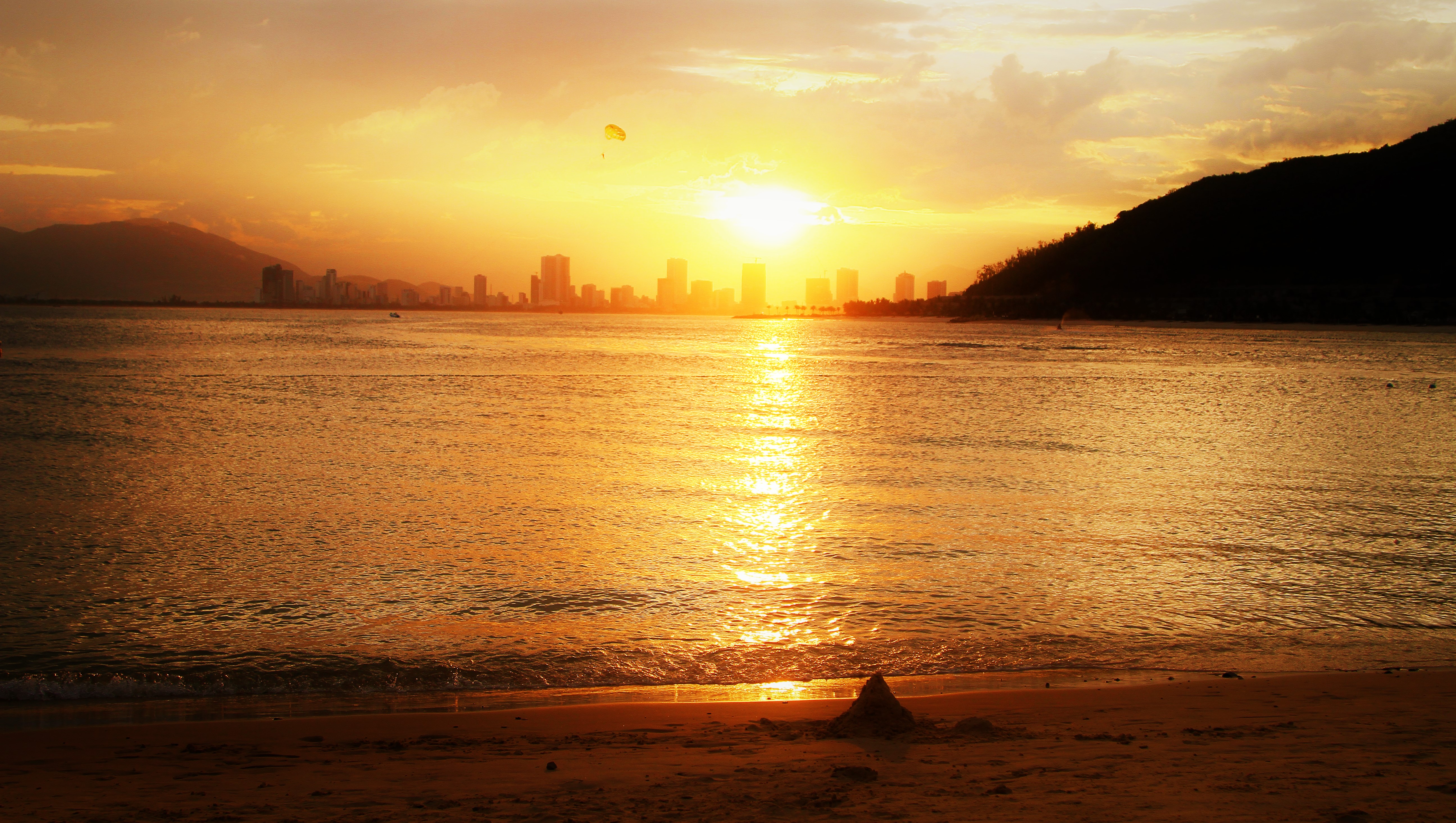 Sunset over the sea with a city skyline and mountains HD Wallpaper