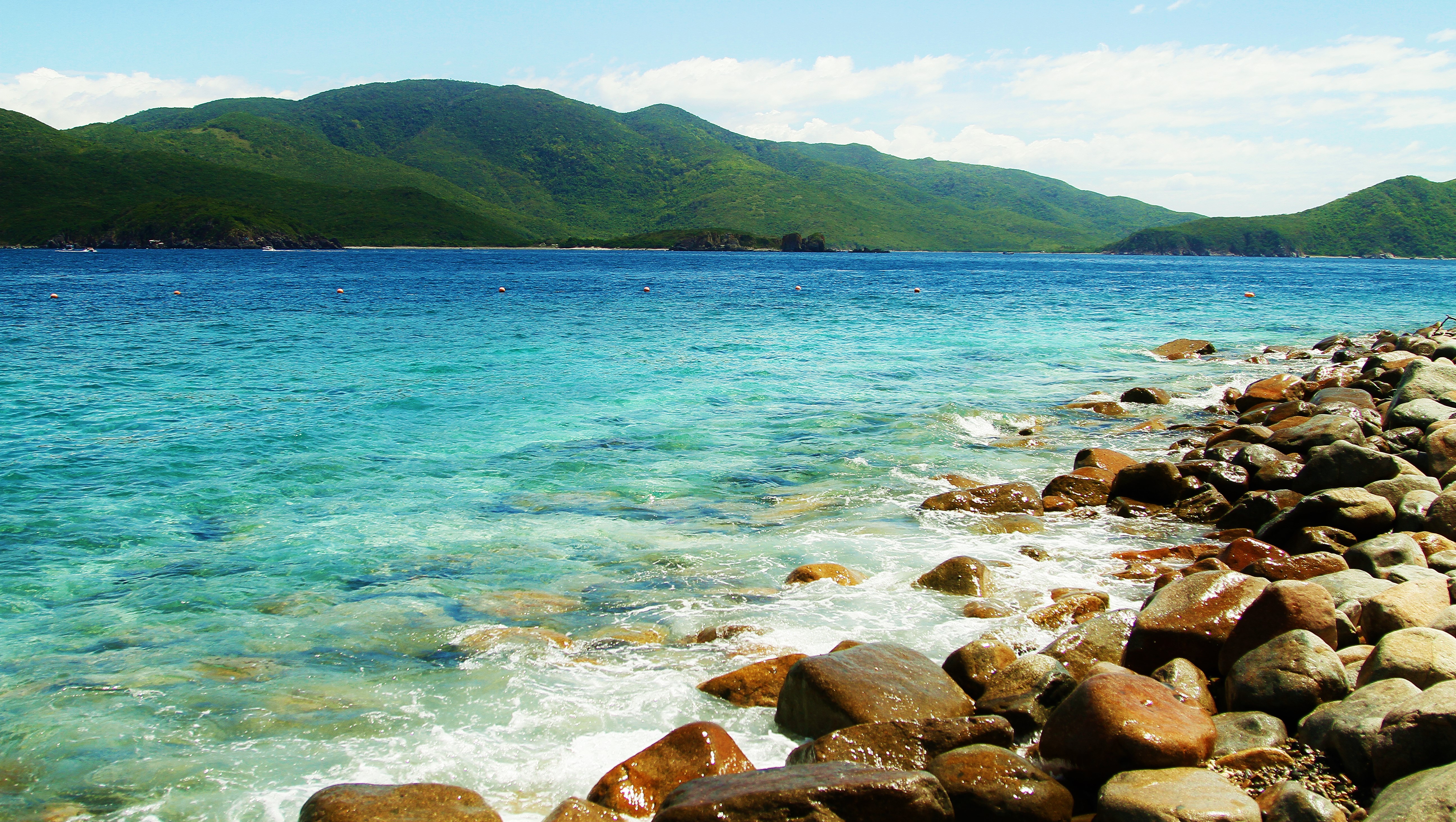 Rocky beach with turquoise water and green mountains HD Wallpaper