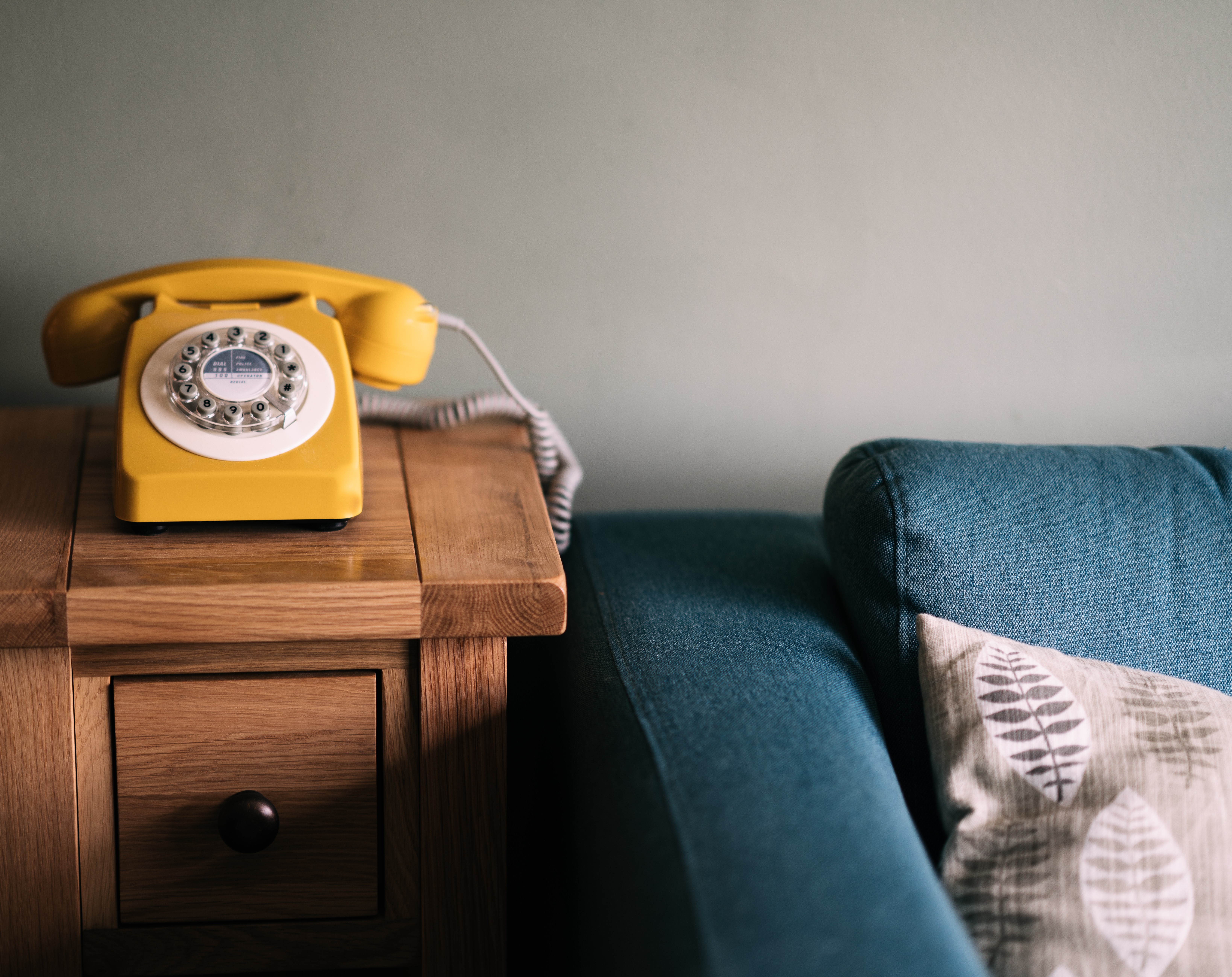Yellow rotary phone on a wooden table next to a sofa HD Wallpaper