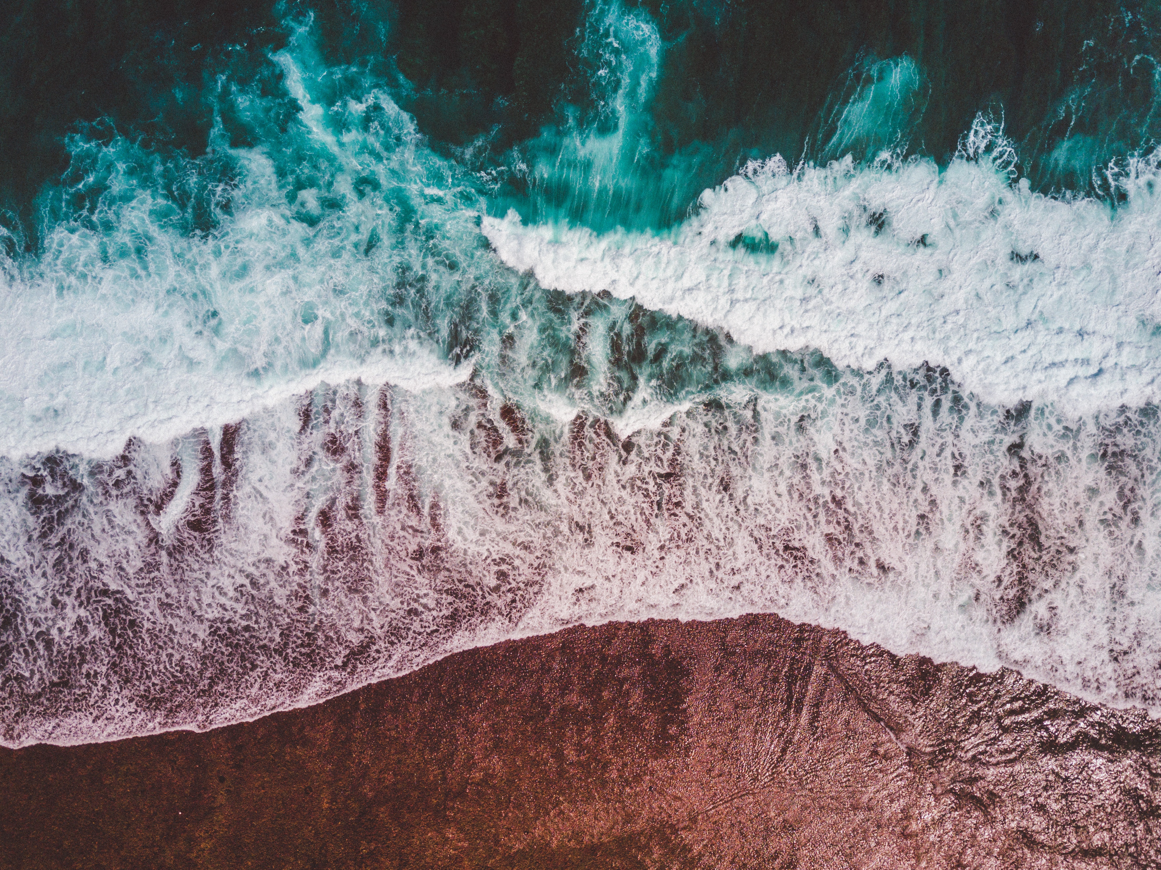 Aerial view of ocean waves crashing on a rocky shore HD Wallpaper
