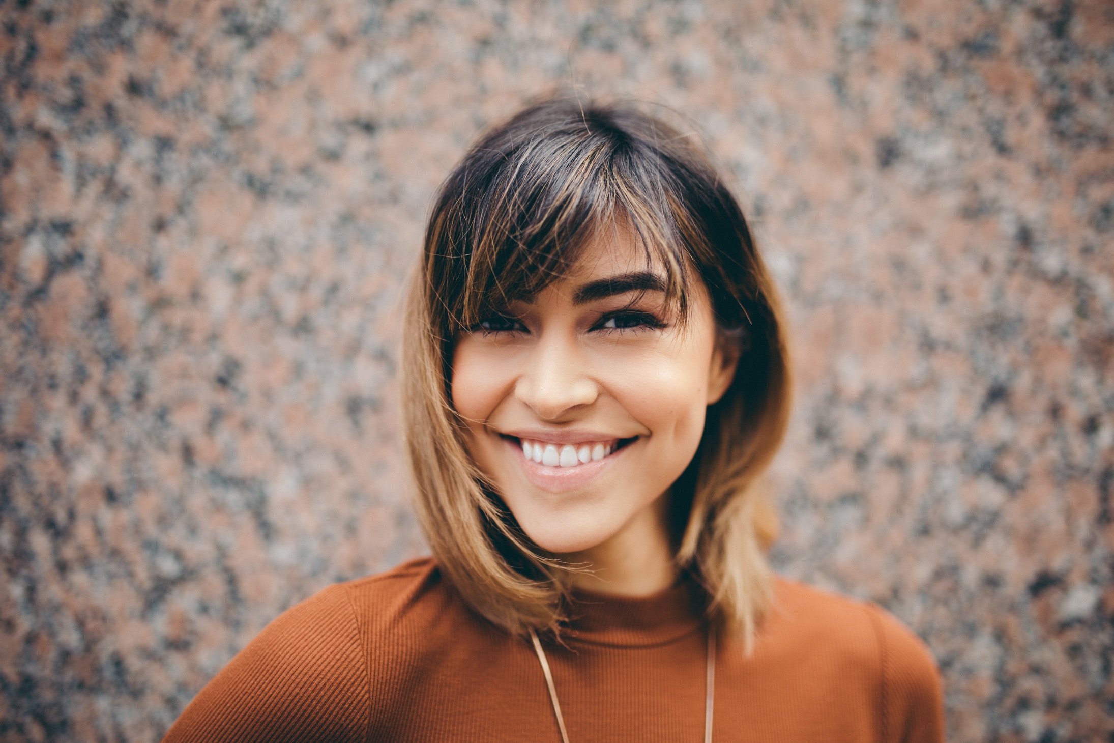 Woman with bangs smiling in front of a speckled wall HD Wallpaper