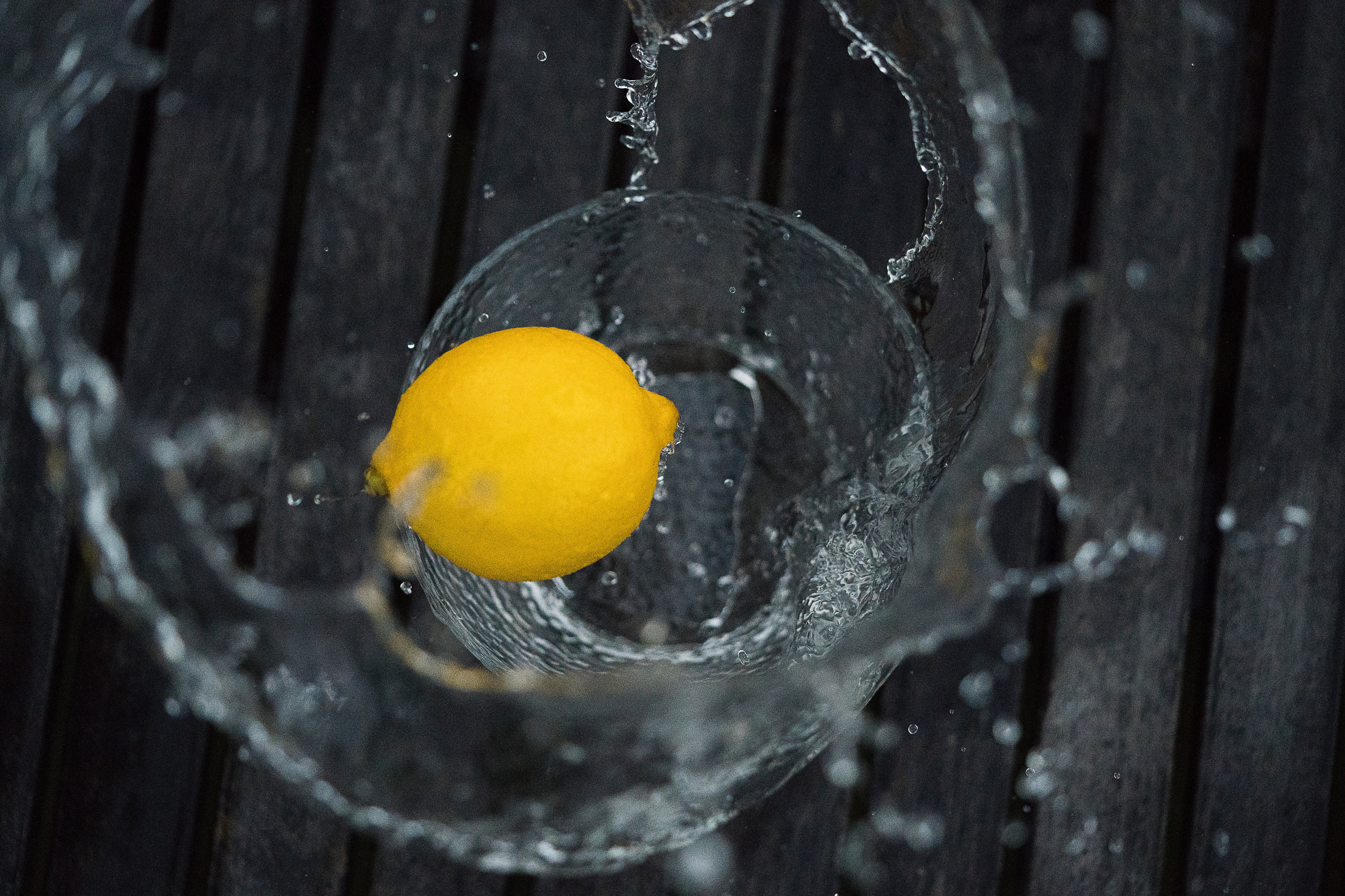 Lemon splashing into a glass on a wooden table HD Wallpaper