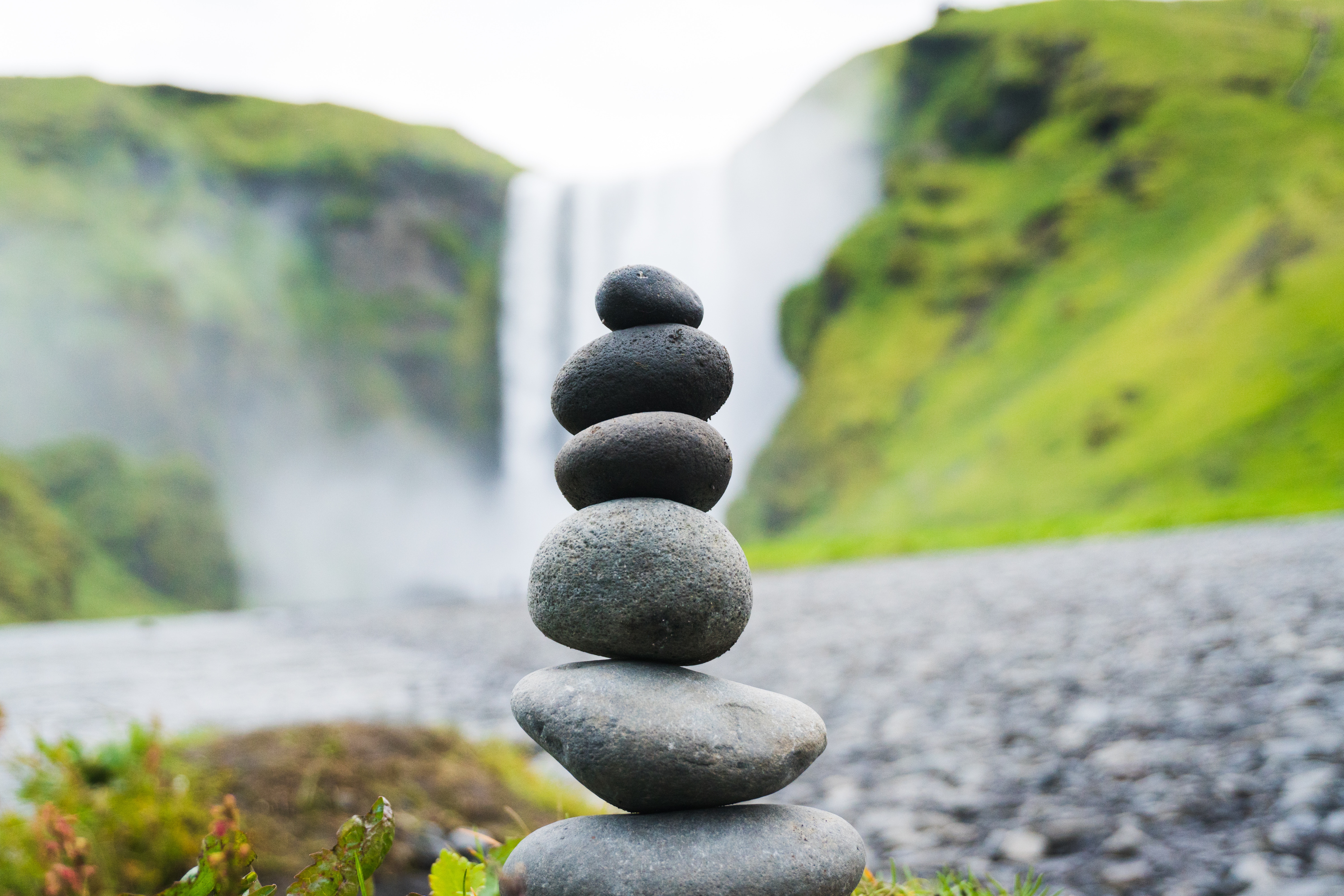 Stack of stones in front of a waterfall HD Wallpaper