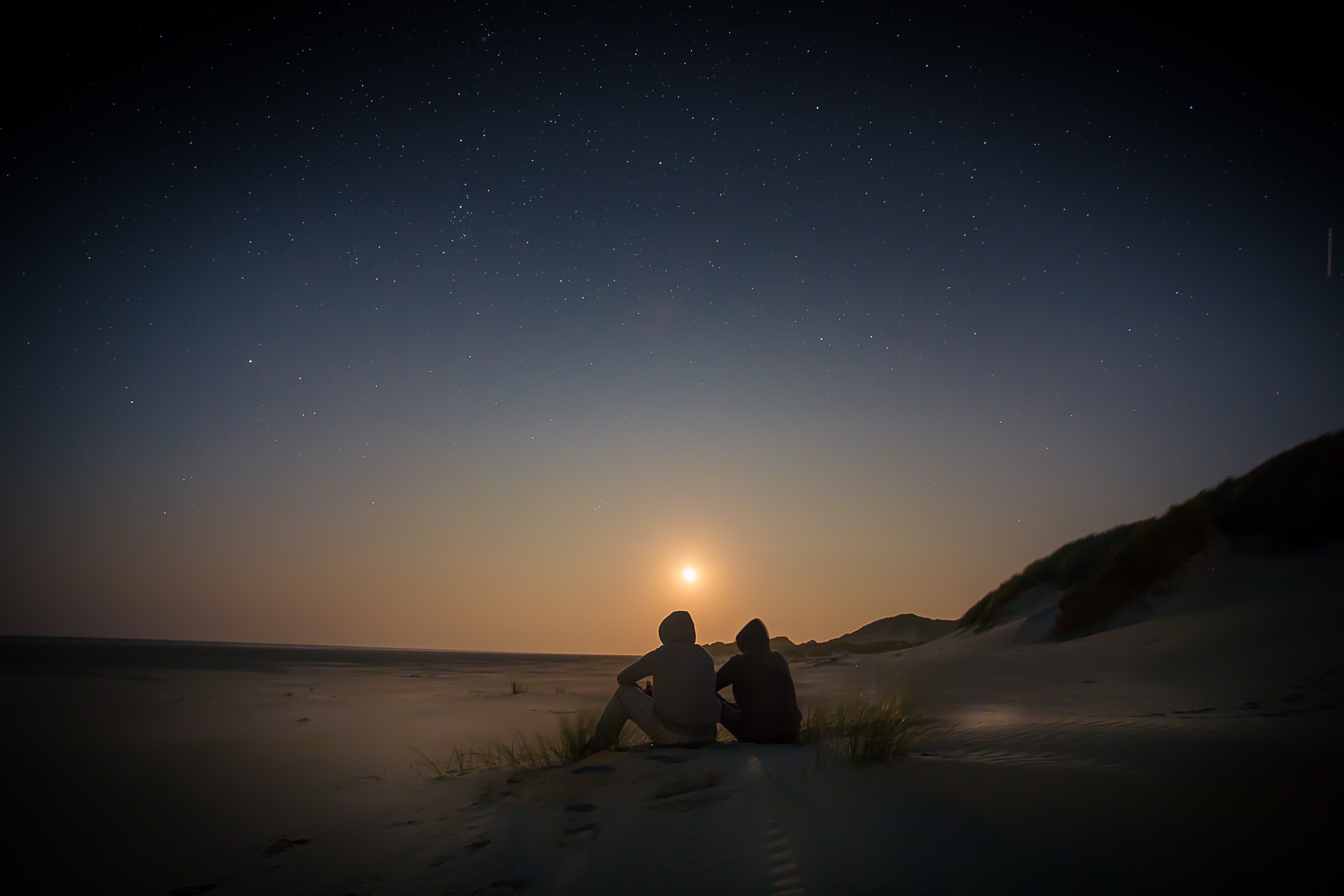 Two people watching the moonrise over a sandy beach HD Wallpaper