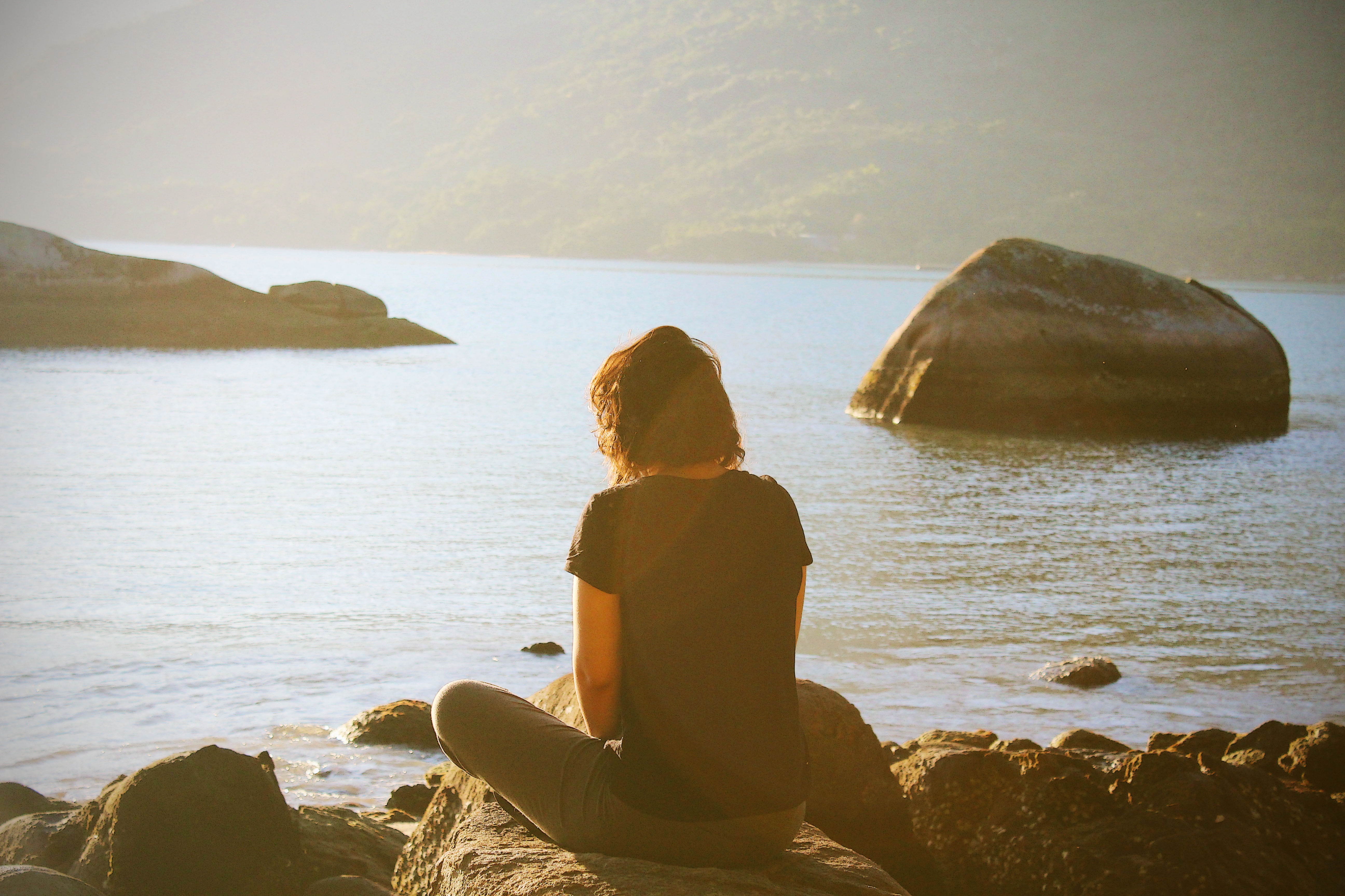 Woman sitting on rocks by the ocean at sunset HD Wallpaper