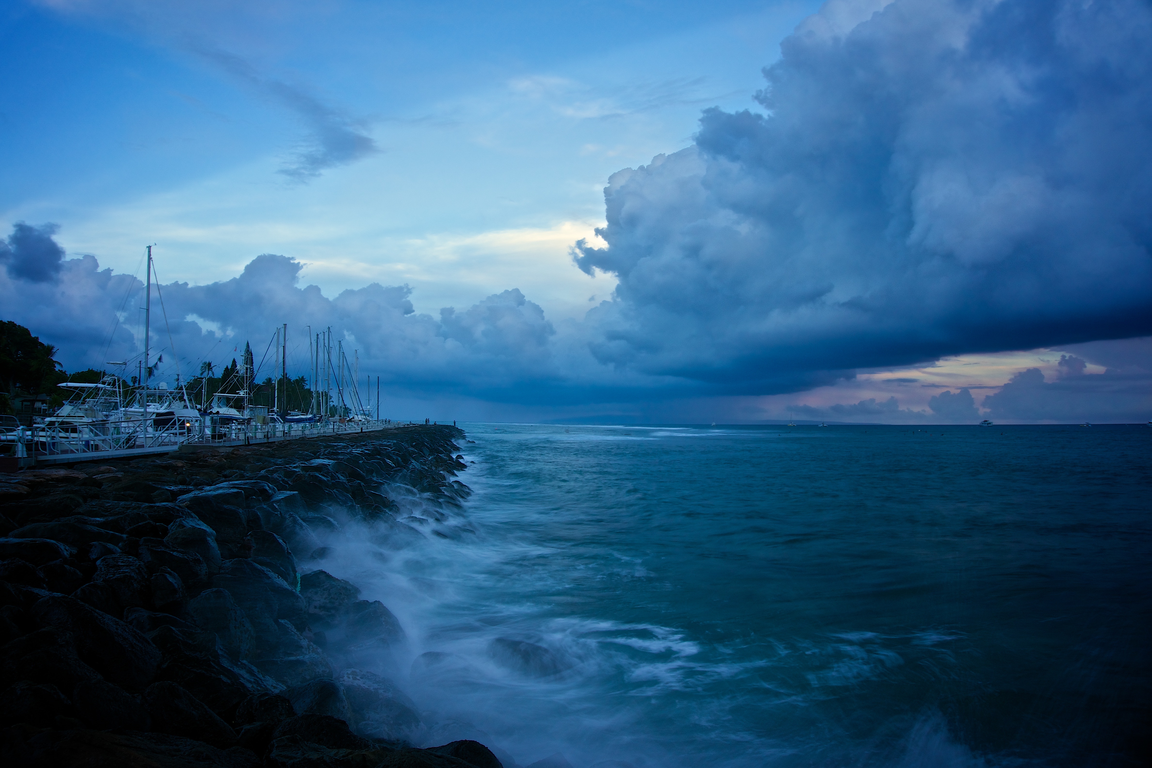 Ocean waves crashing on a rocky coast with boats at dusk HD Wallpaper