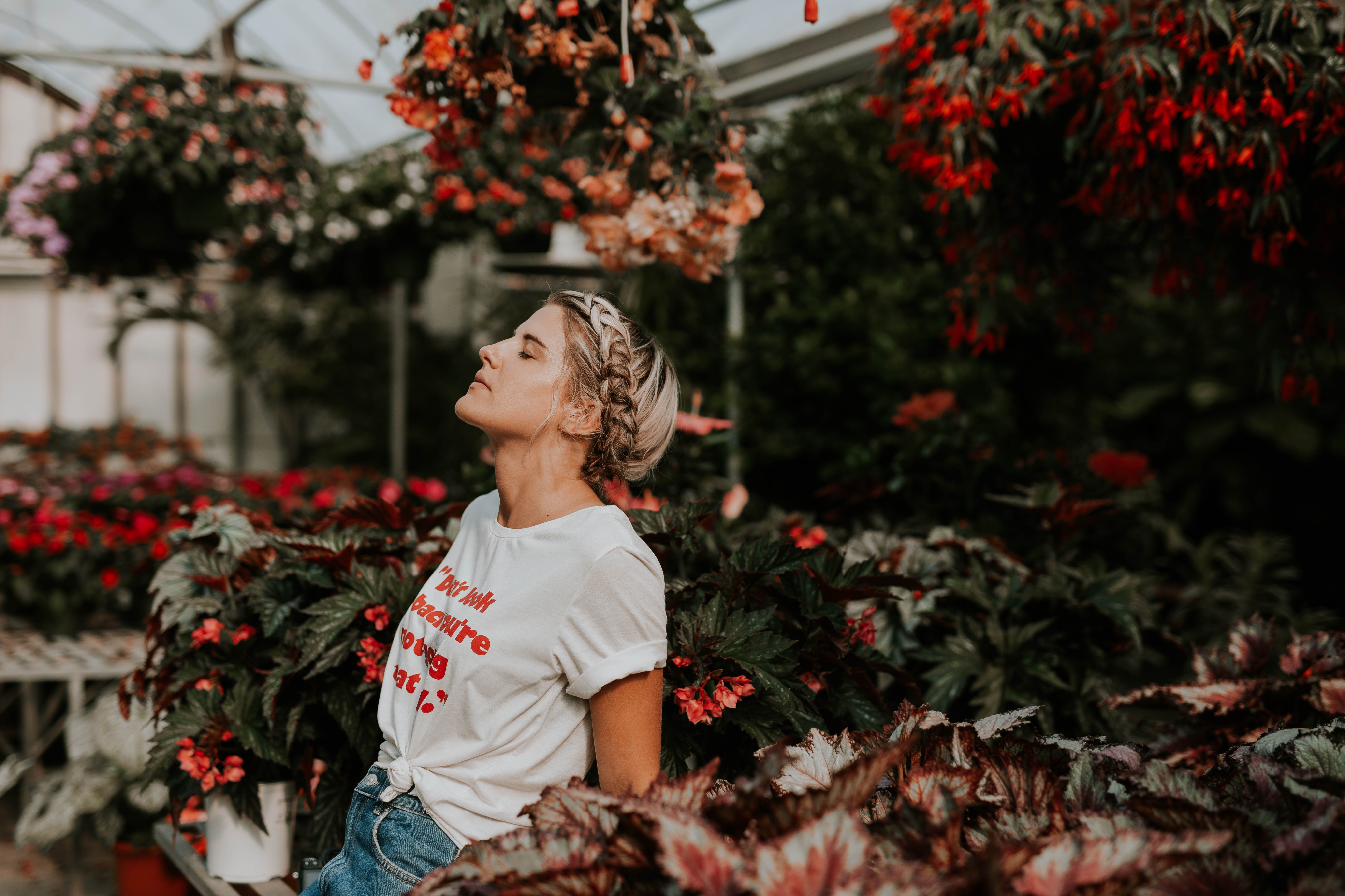 Woman with eyes closed in a greenhouse with flowers HD Wallpaper