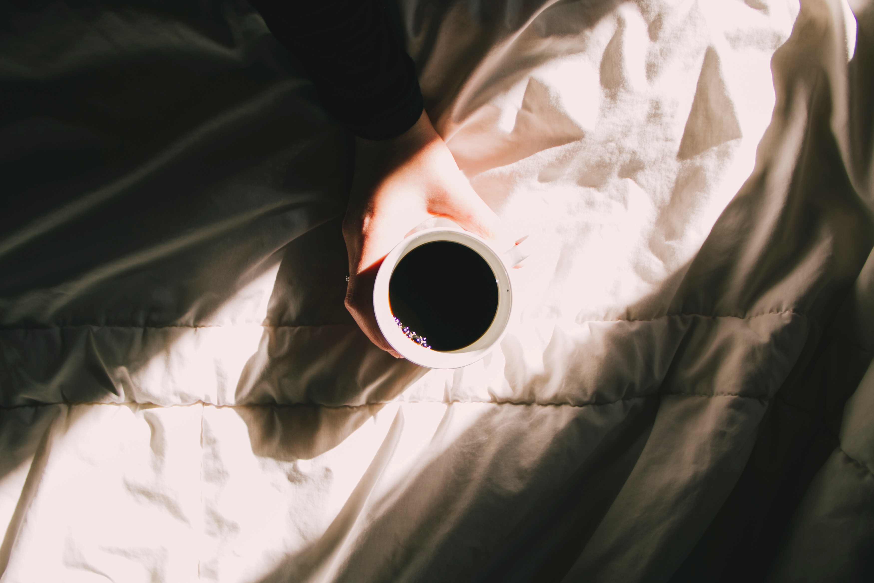 Hand holding a cup of black coffee on a bed HD Wallpaper