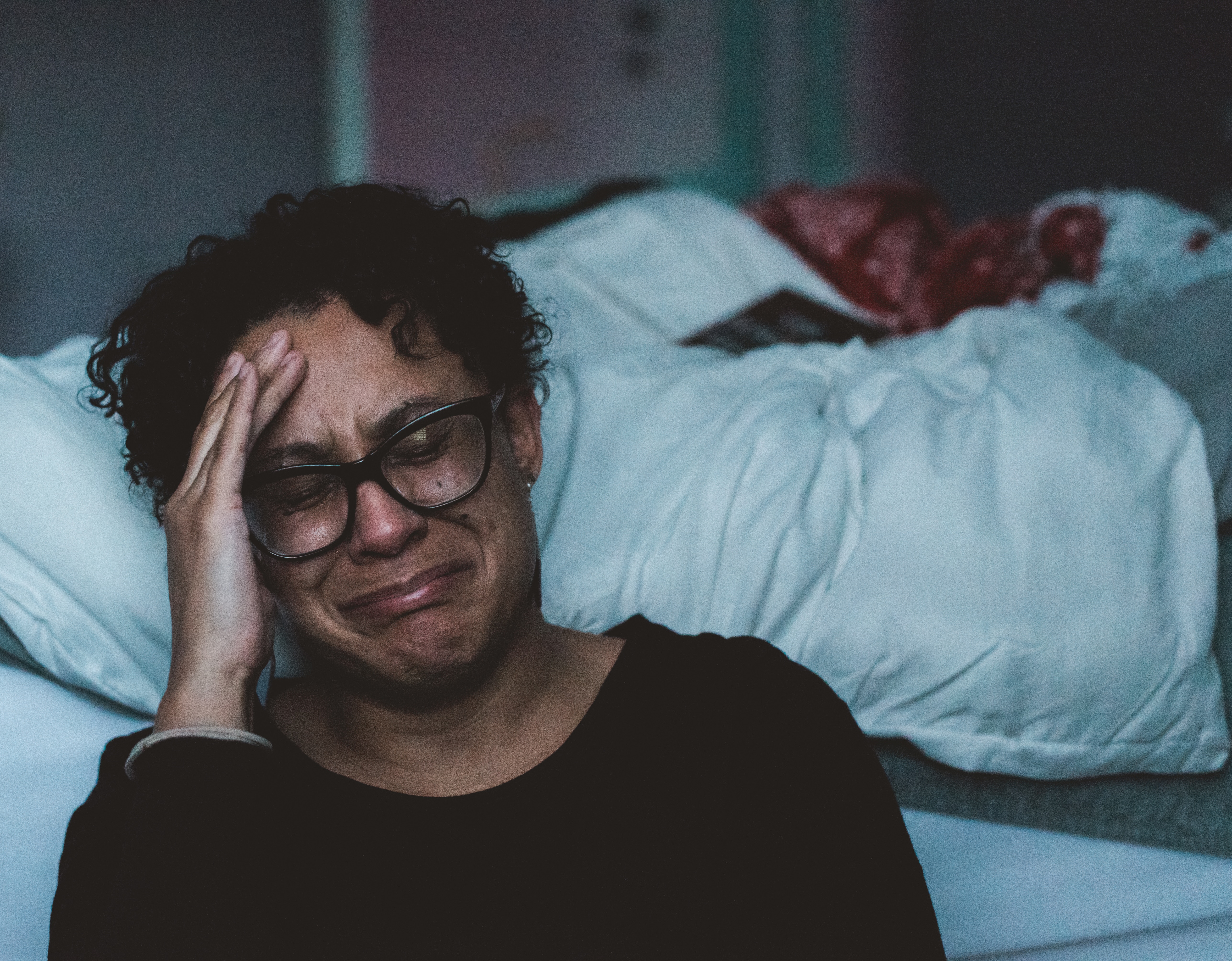 Woman with glasses crying on a bed HD Wallpaper