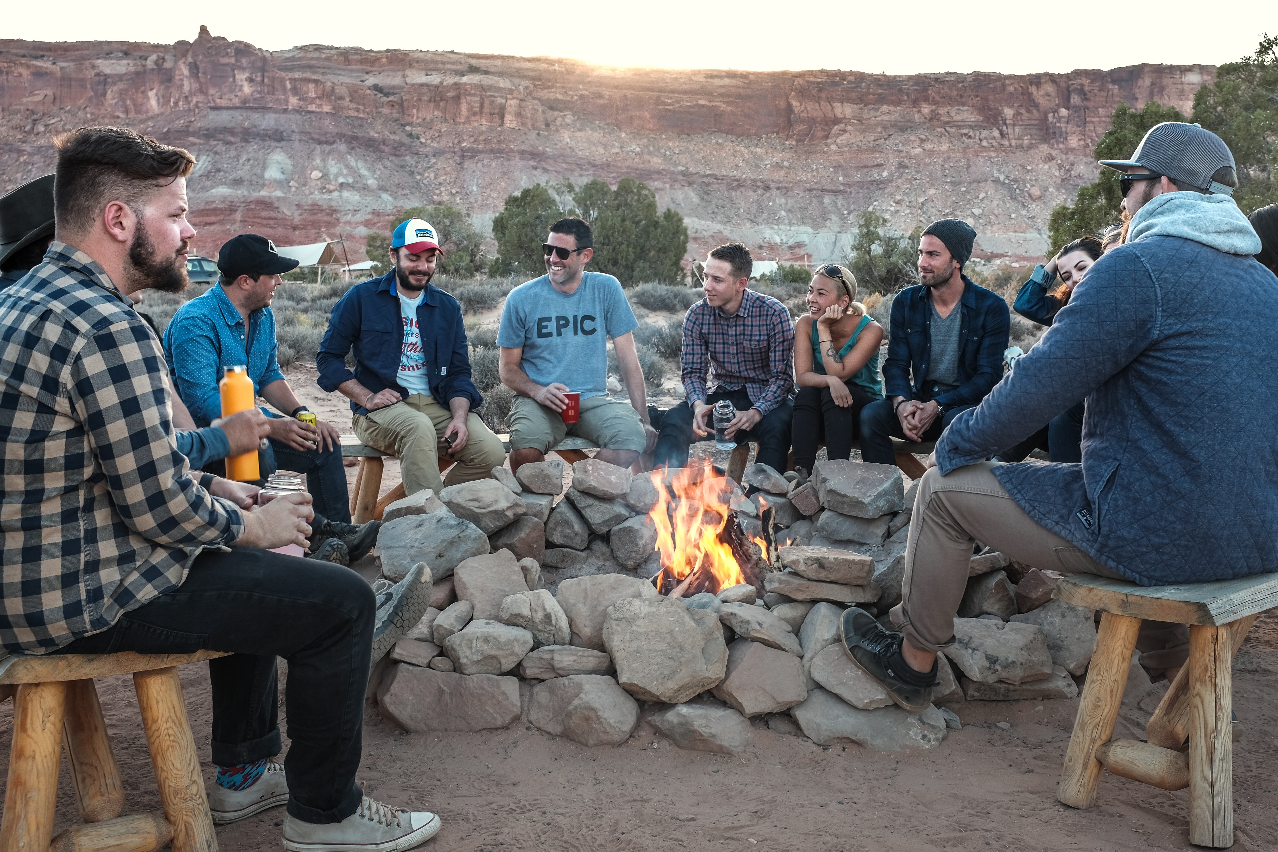 Group of friends gathered around a campfire at sunset HD Wallpaper