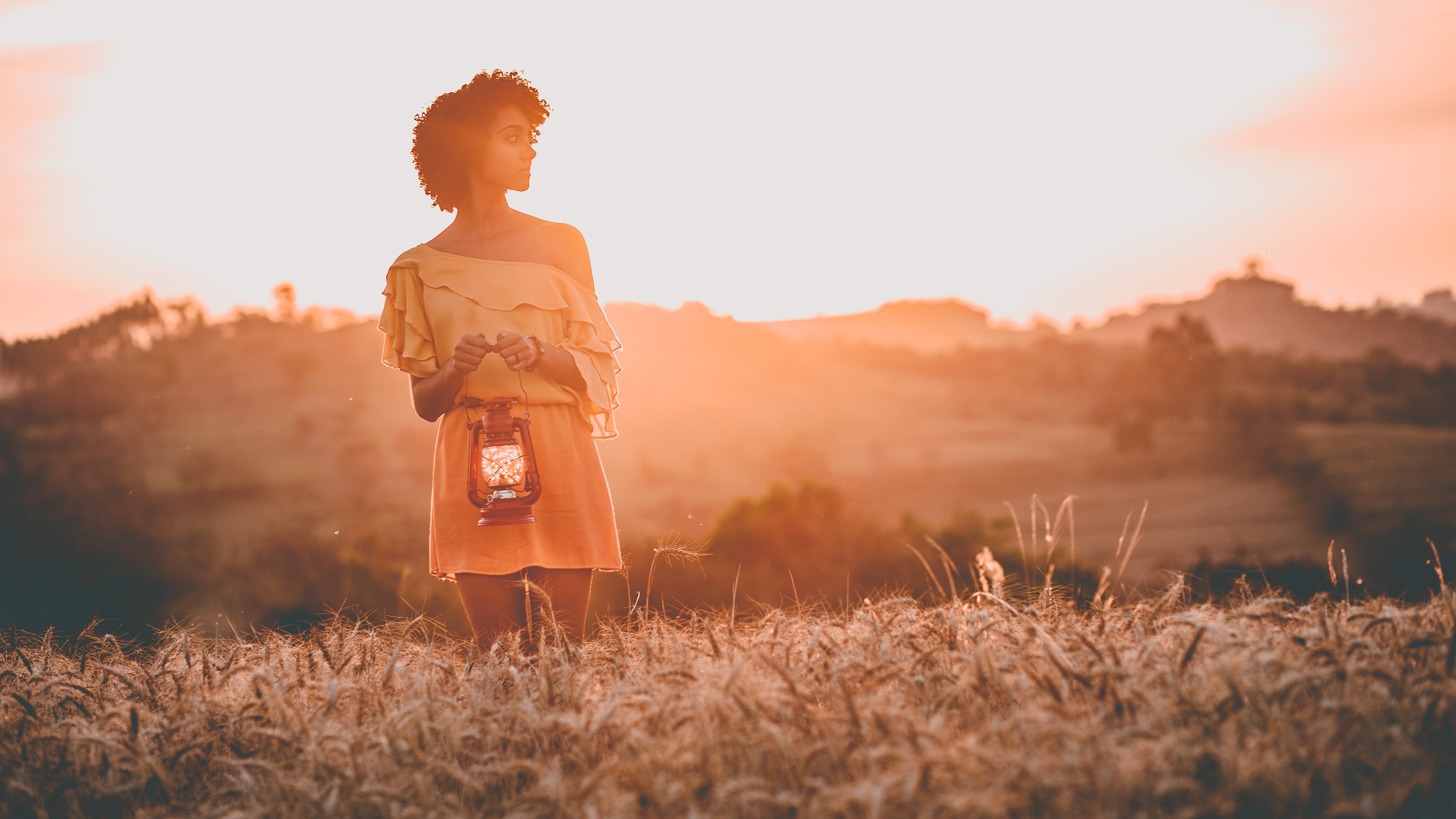 Woman holding a lantern in a field at sunset HD Wallpaper
