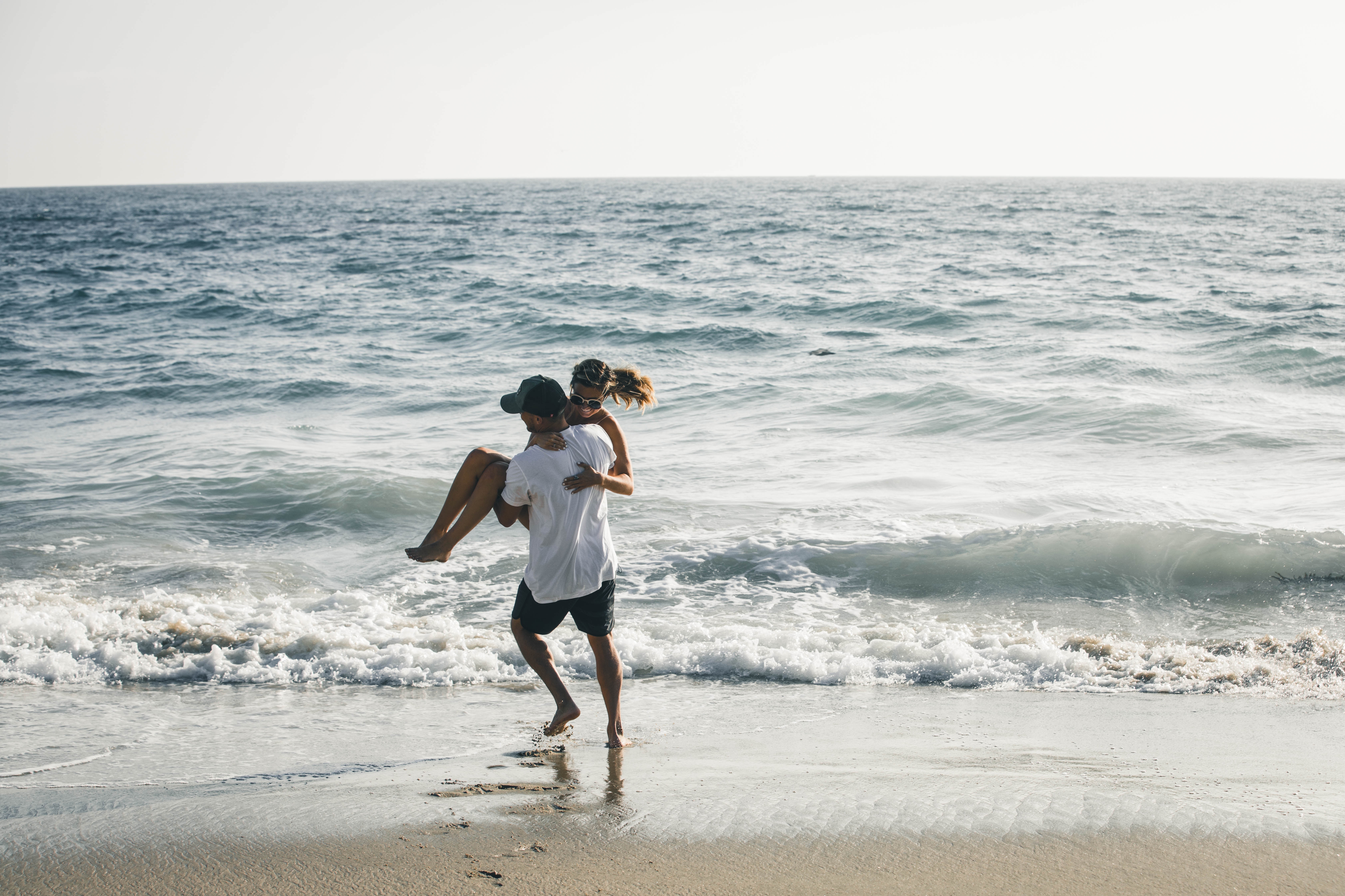Couple playing in the ocean waves at the beach HD Wallpaper