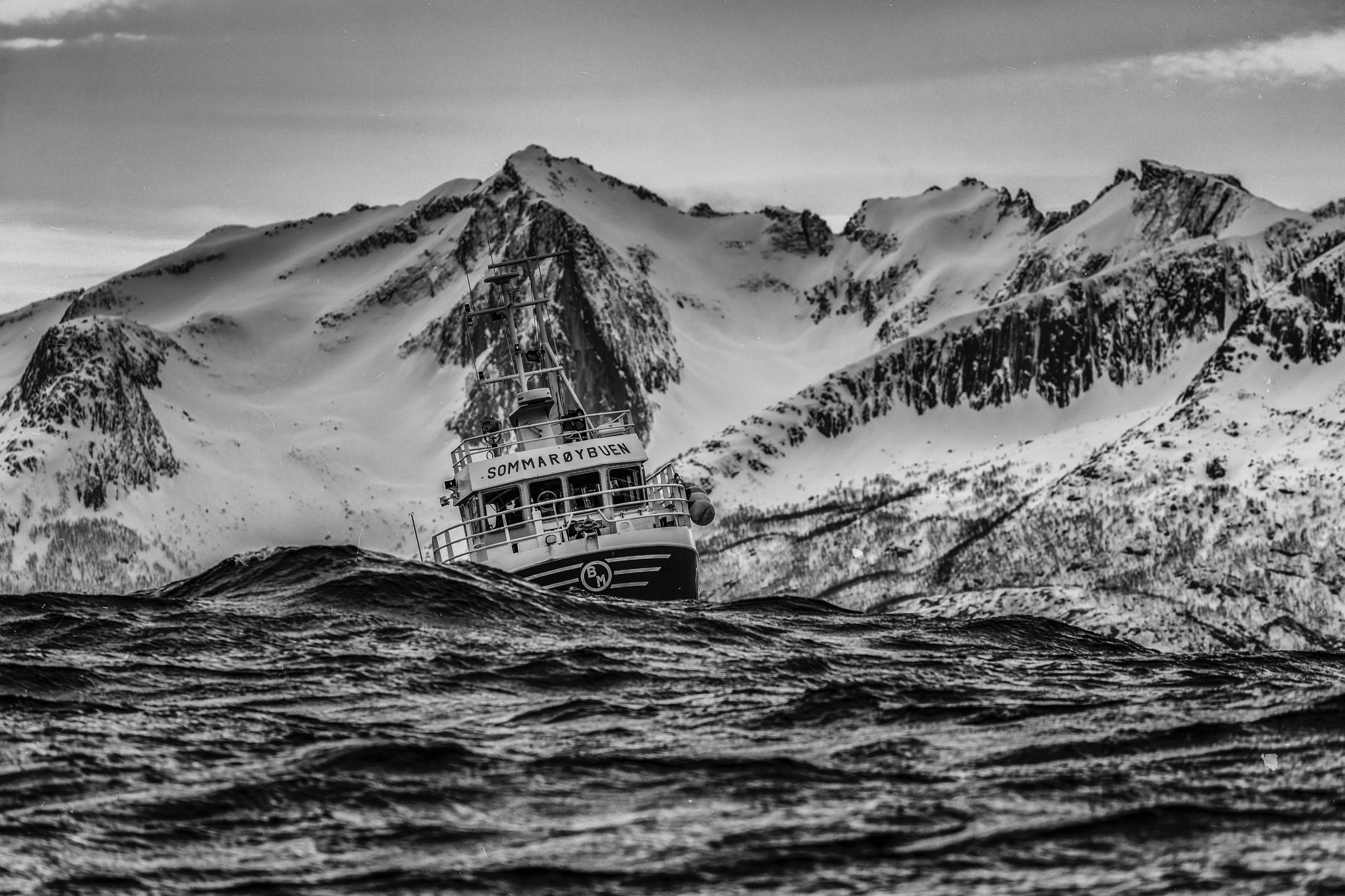 Fishing boat on a rough sea with snow-capped mountains HD Wallpaper
