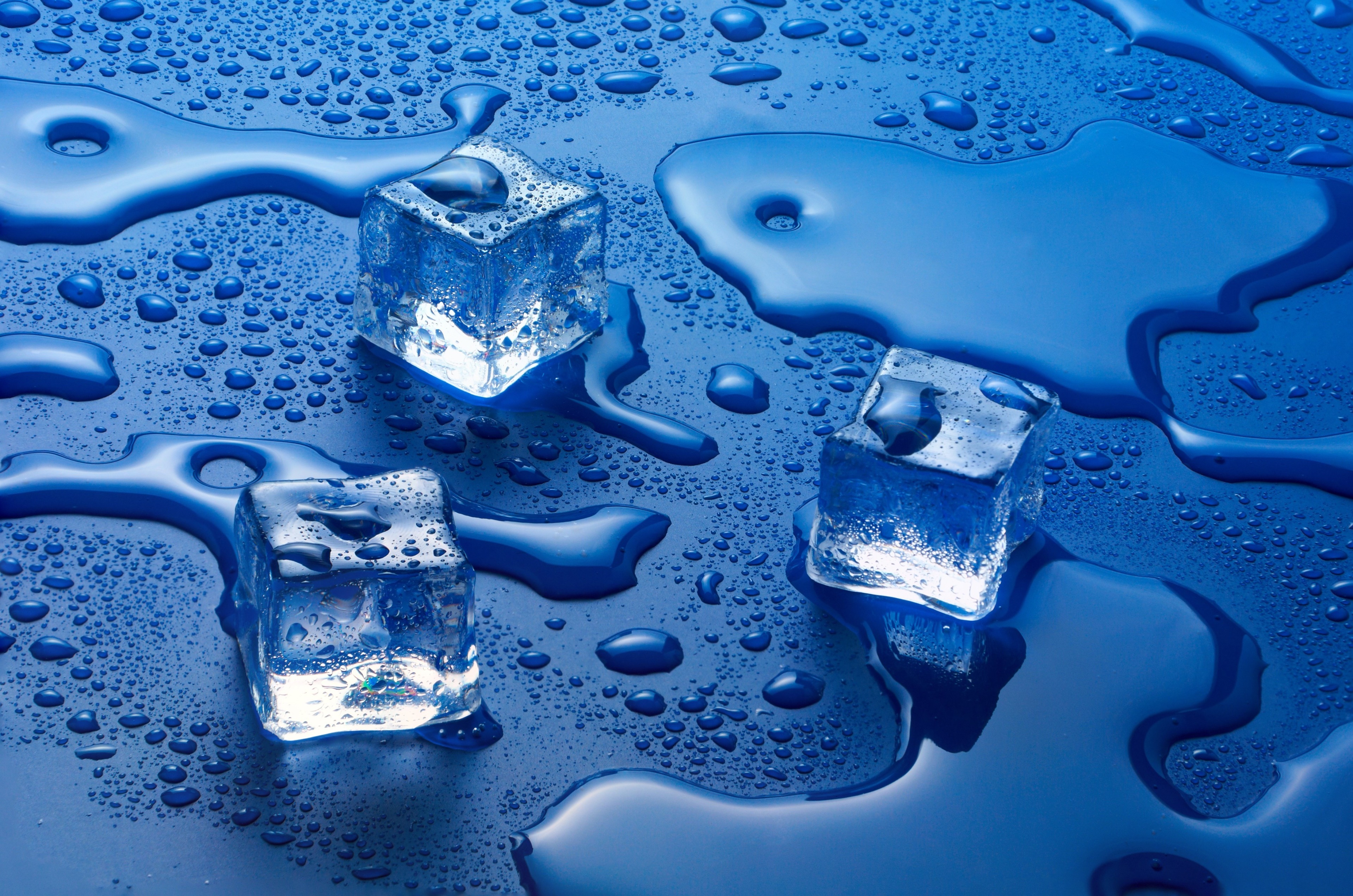 Ice cubes melting on a blue surface with water droplets HD Wallpaper