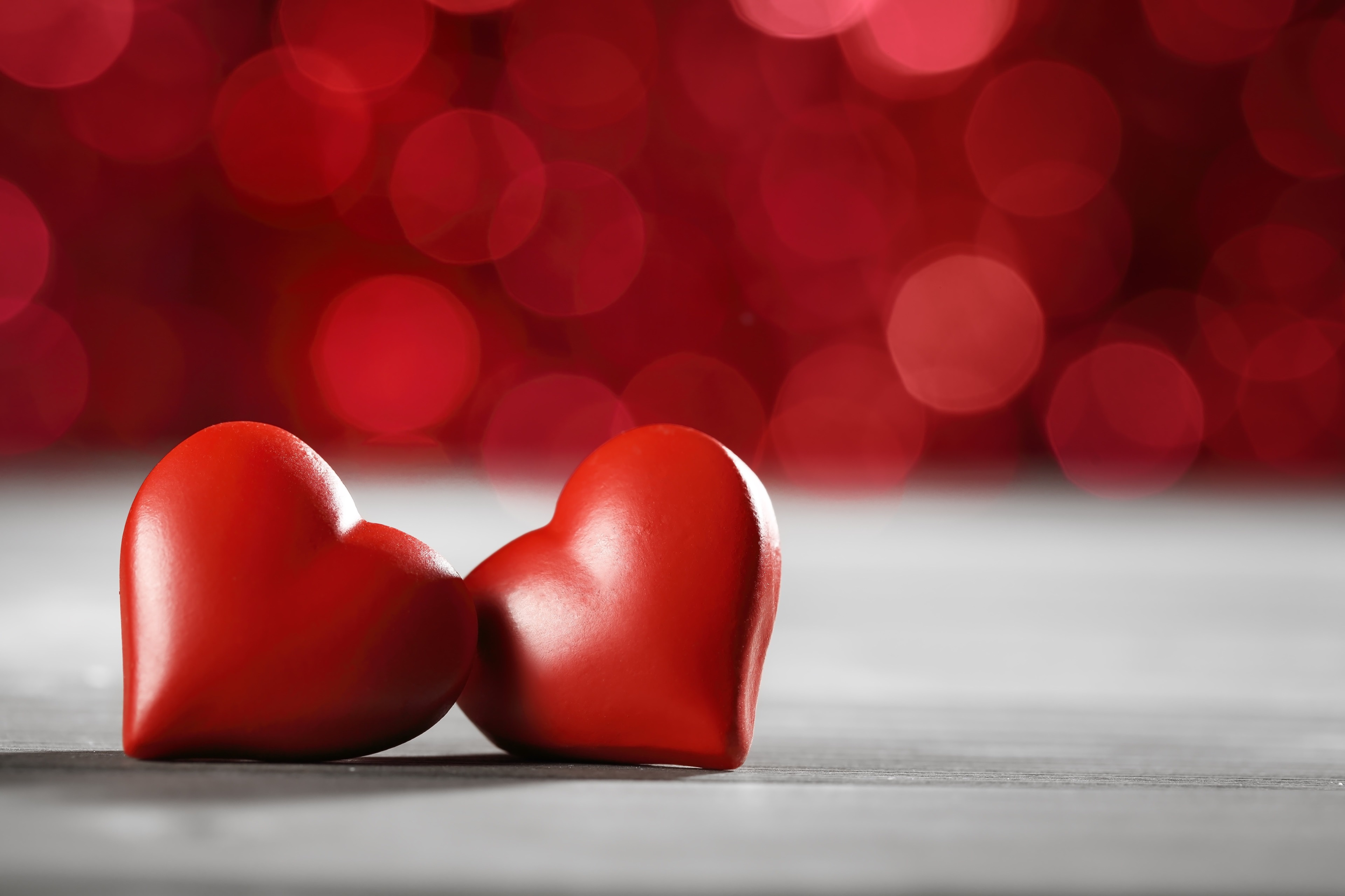 Two red hearts on a wooden surface with bokeh background HD Wallpaper