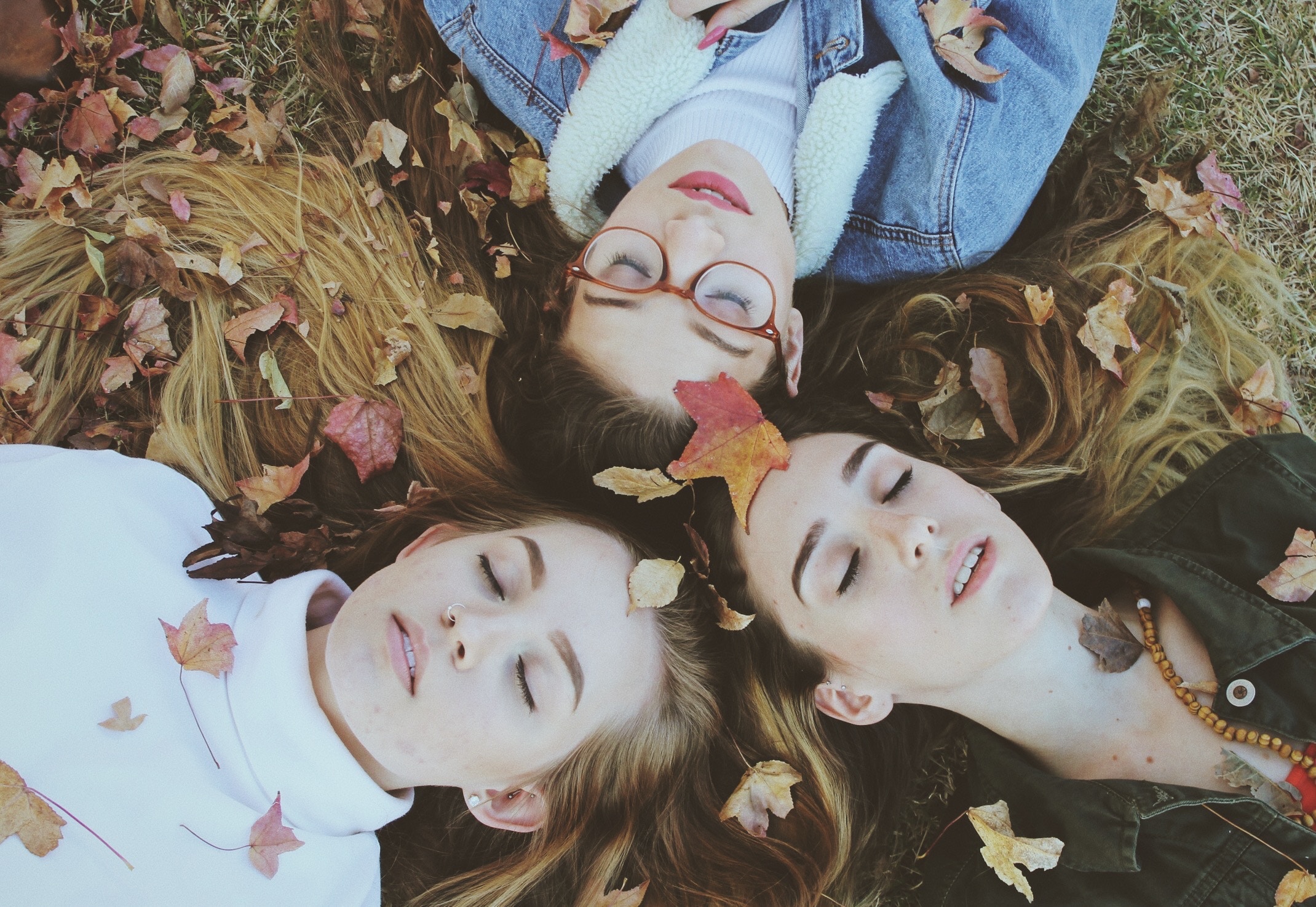 Three young women lying in autumn leaves HD Wallpaper