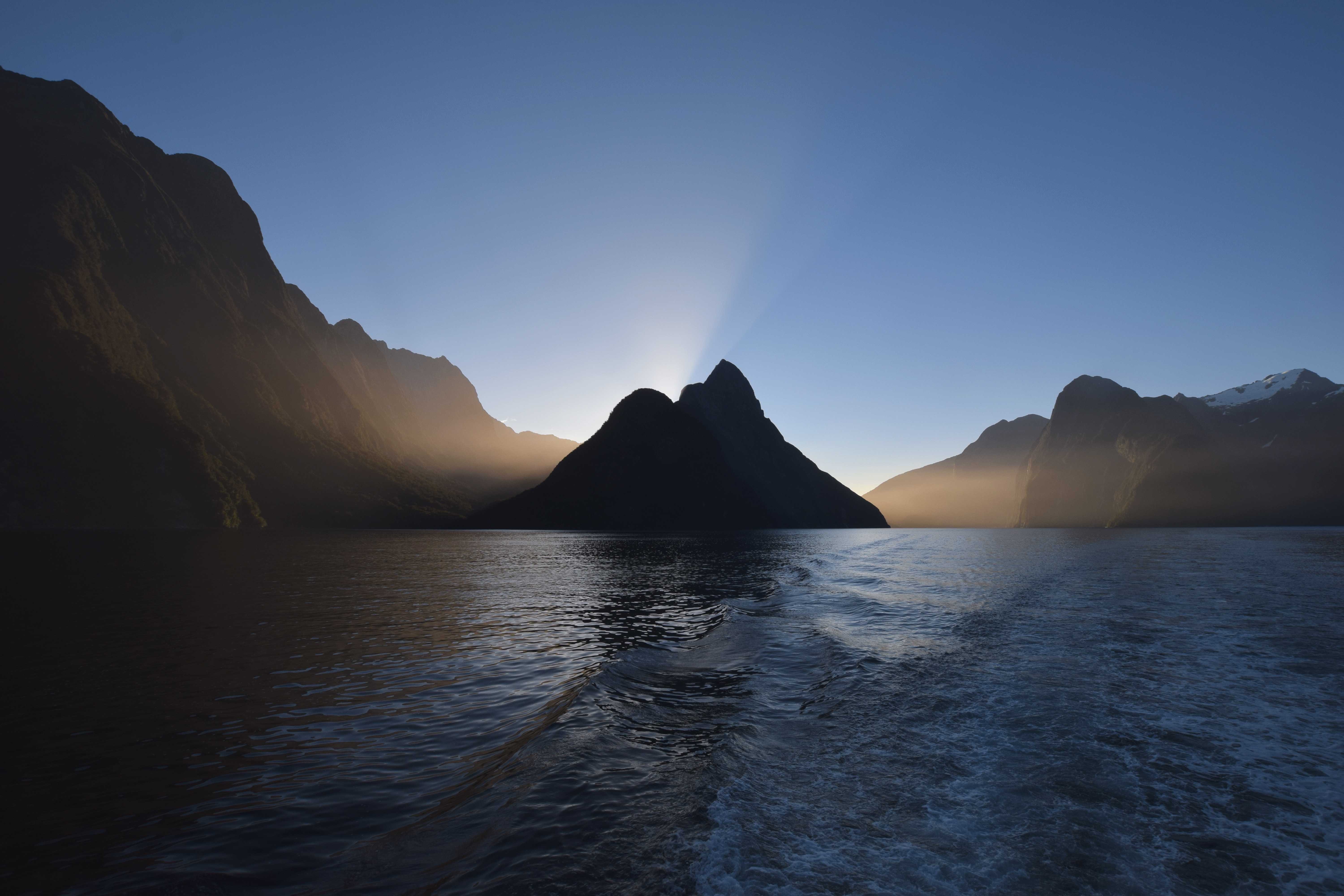 Sun rays behind a mountain in a fjord HD Wallpaper