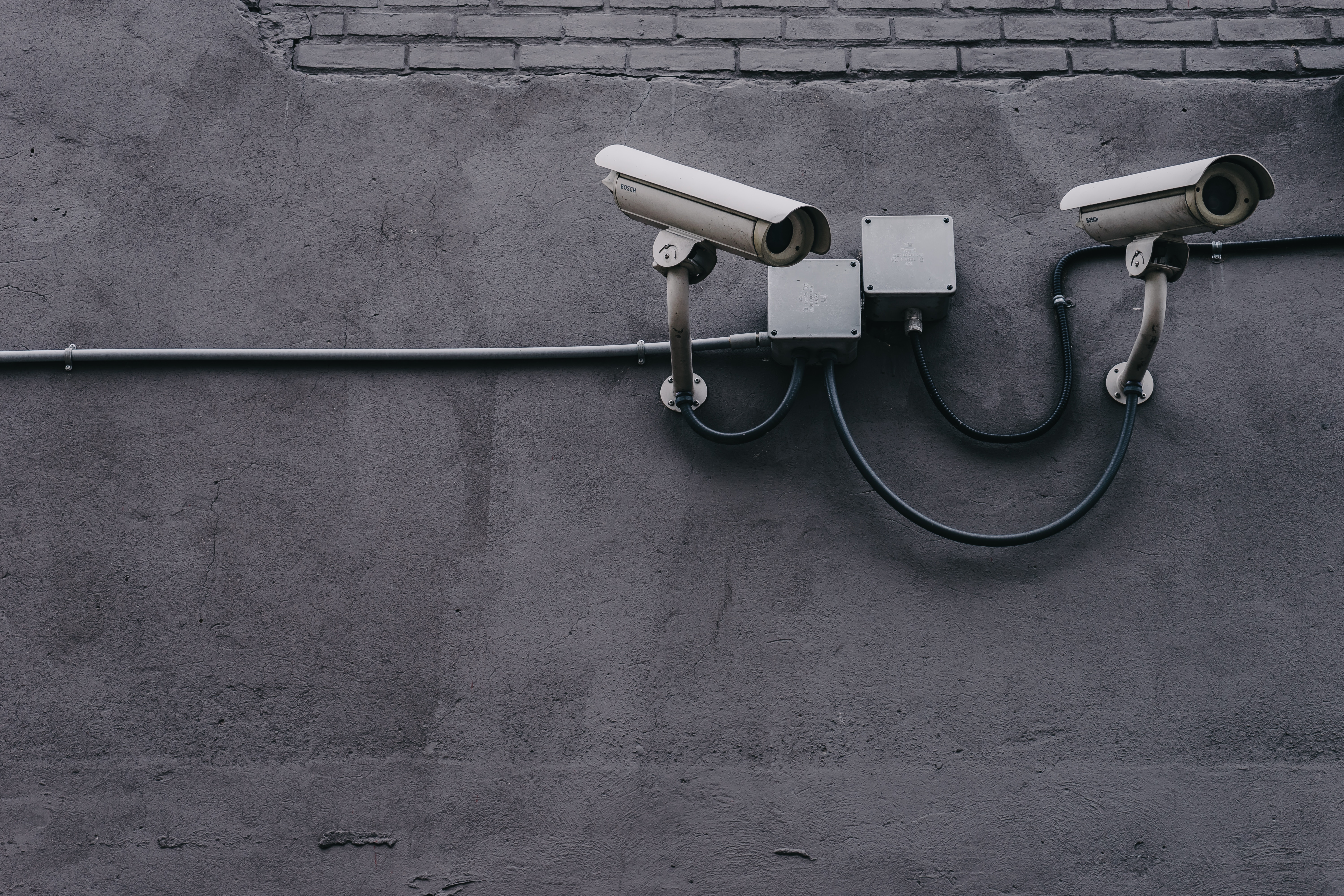Two security cameras mounted on a grey concrete wall HD Wallpaper