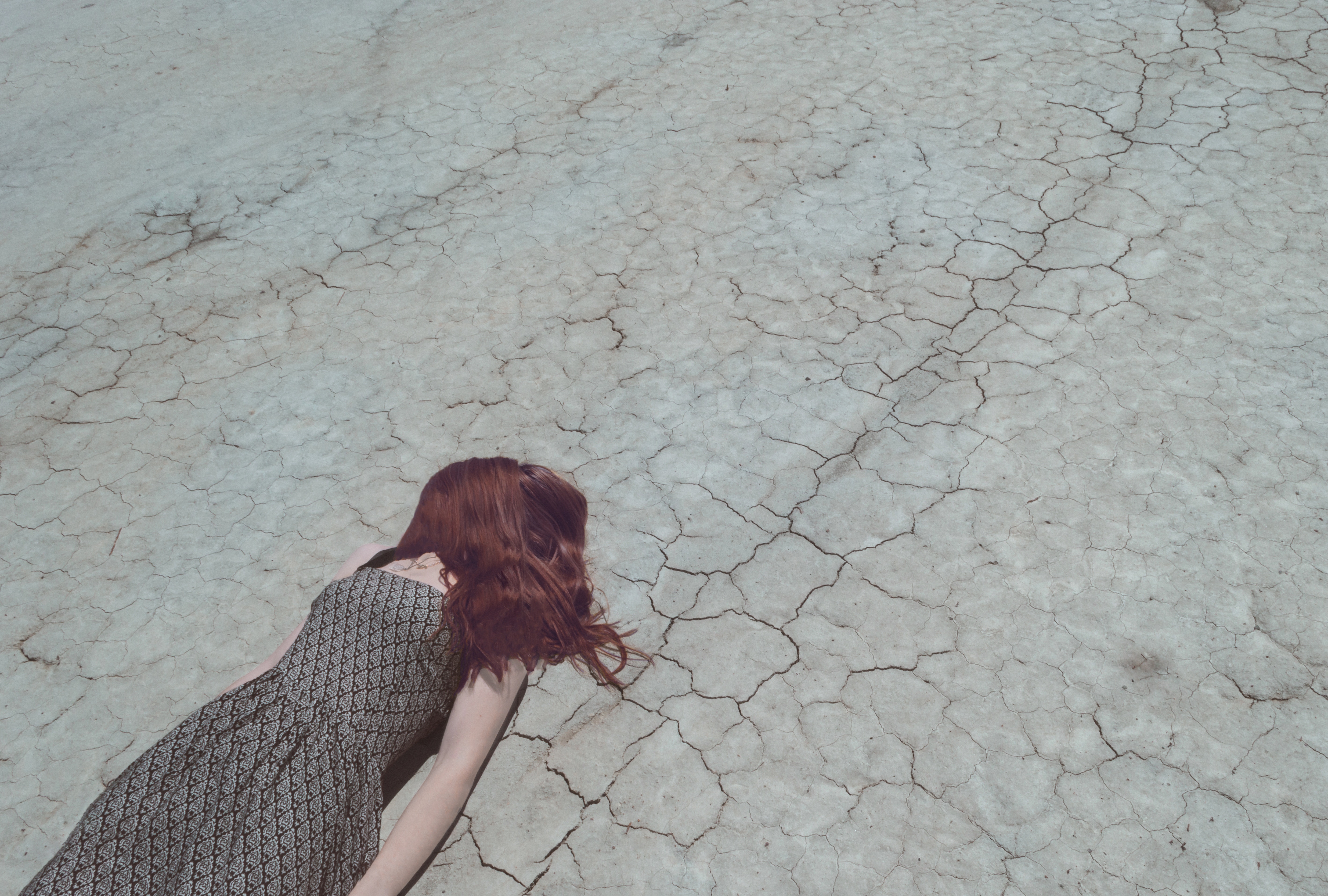 Woman with red hair lying on cracked dry ground HD Wallpaper