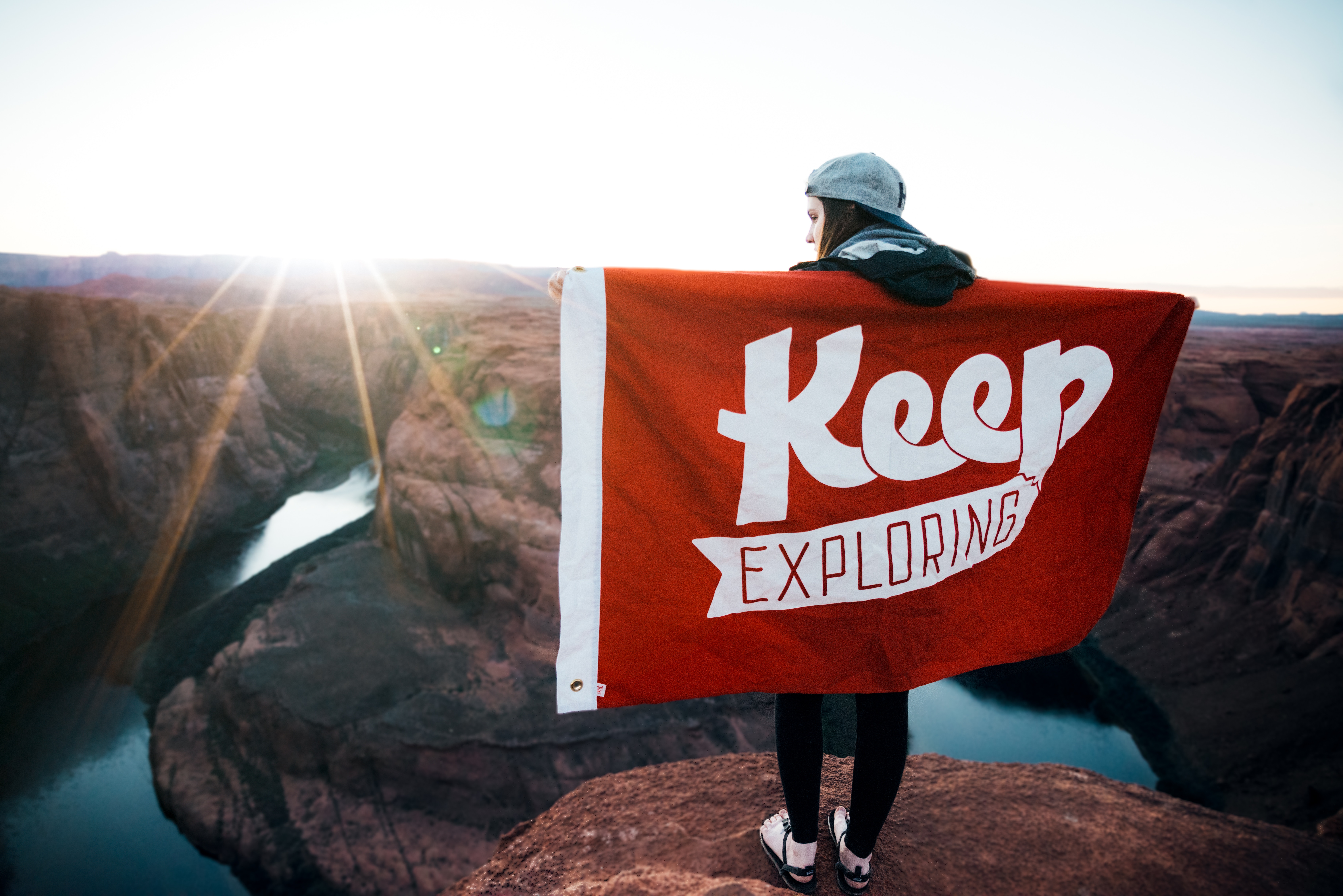 Woman holding a flag with 'Keep Exploring' at Horseshoe Bend HD Wallpaper