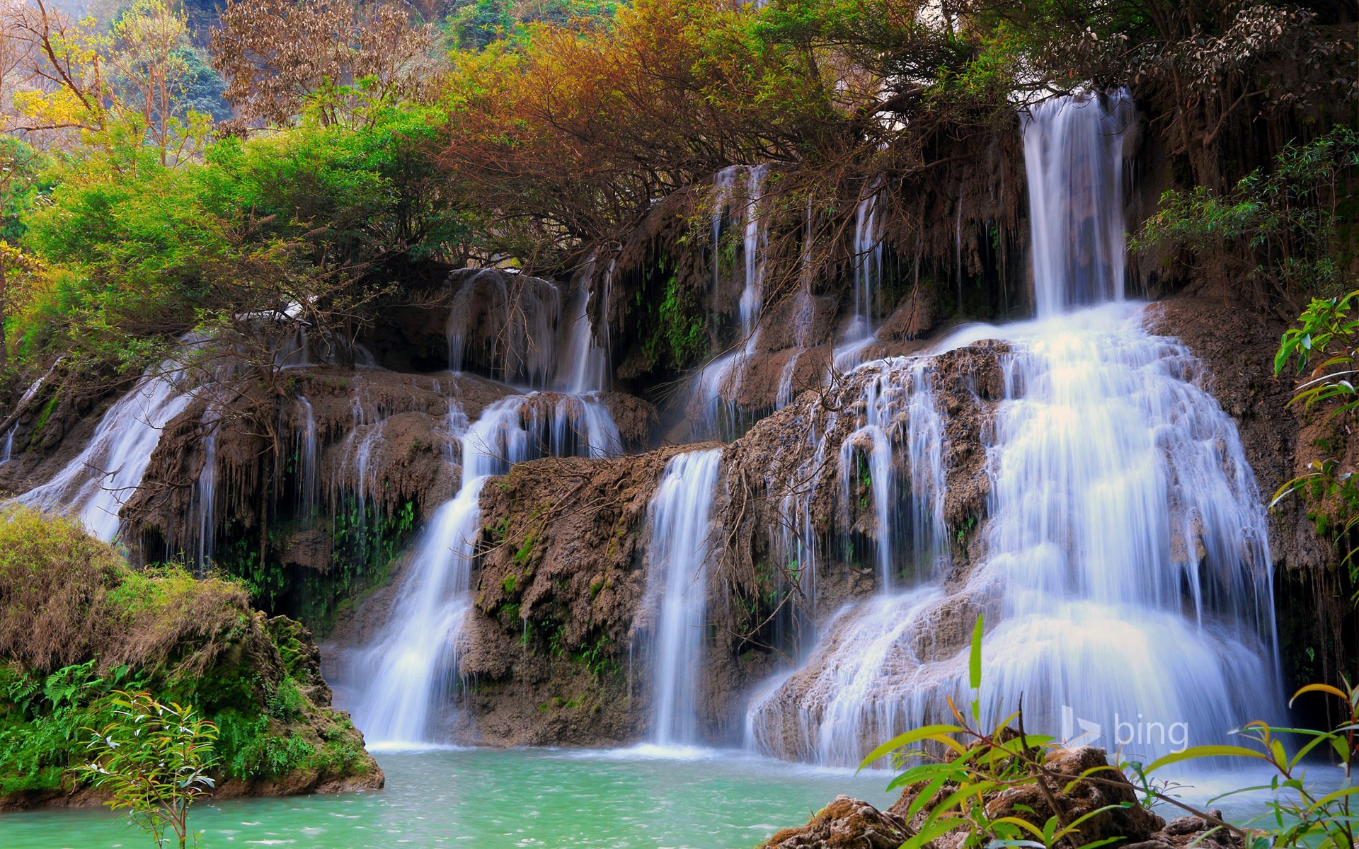 Multi-tiered waterfall cascading into a turquoise pool HD Wallpaper