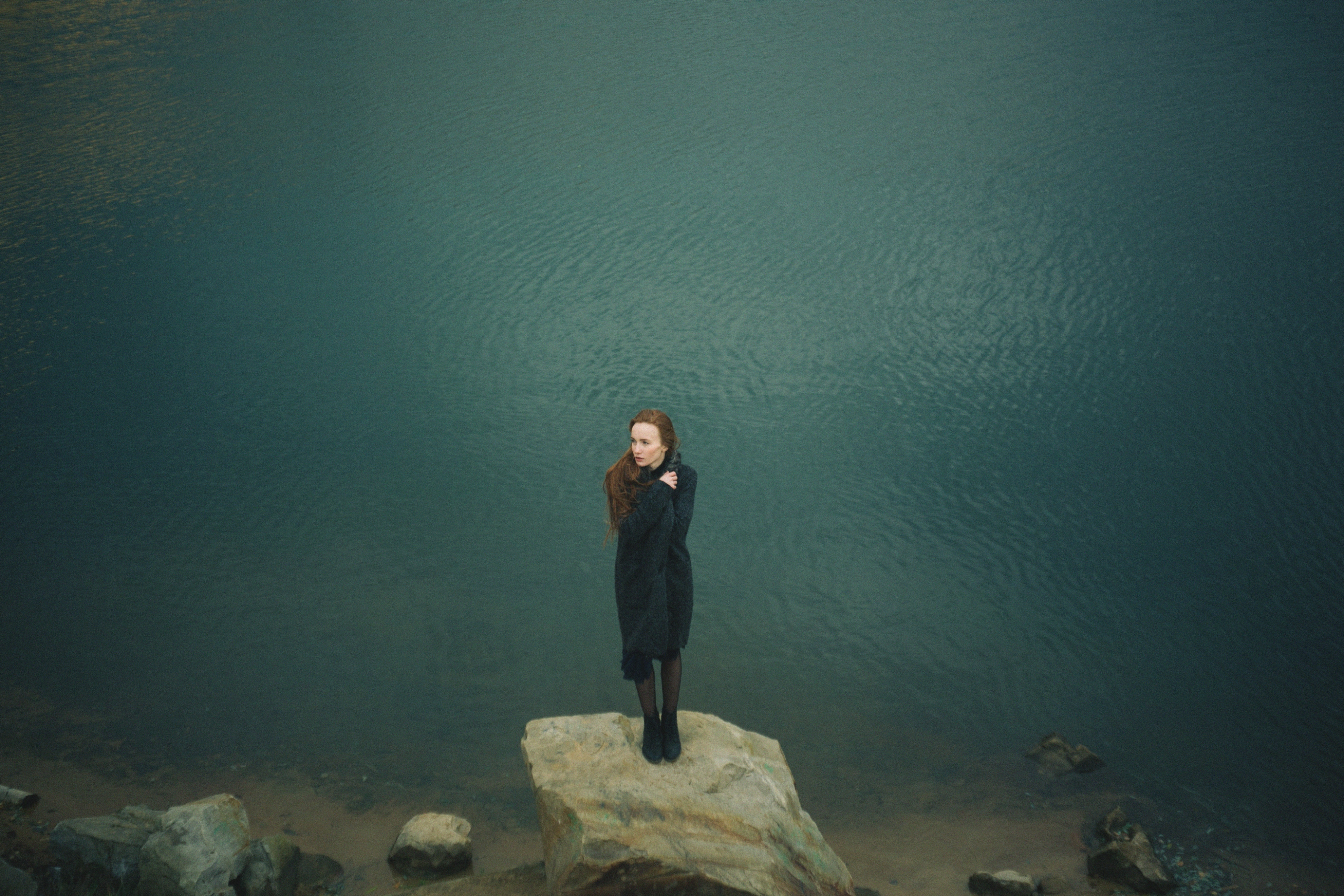 Woman with red hair standing on a rock by the water HD Wallpaper