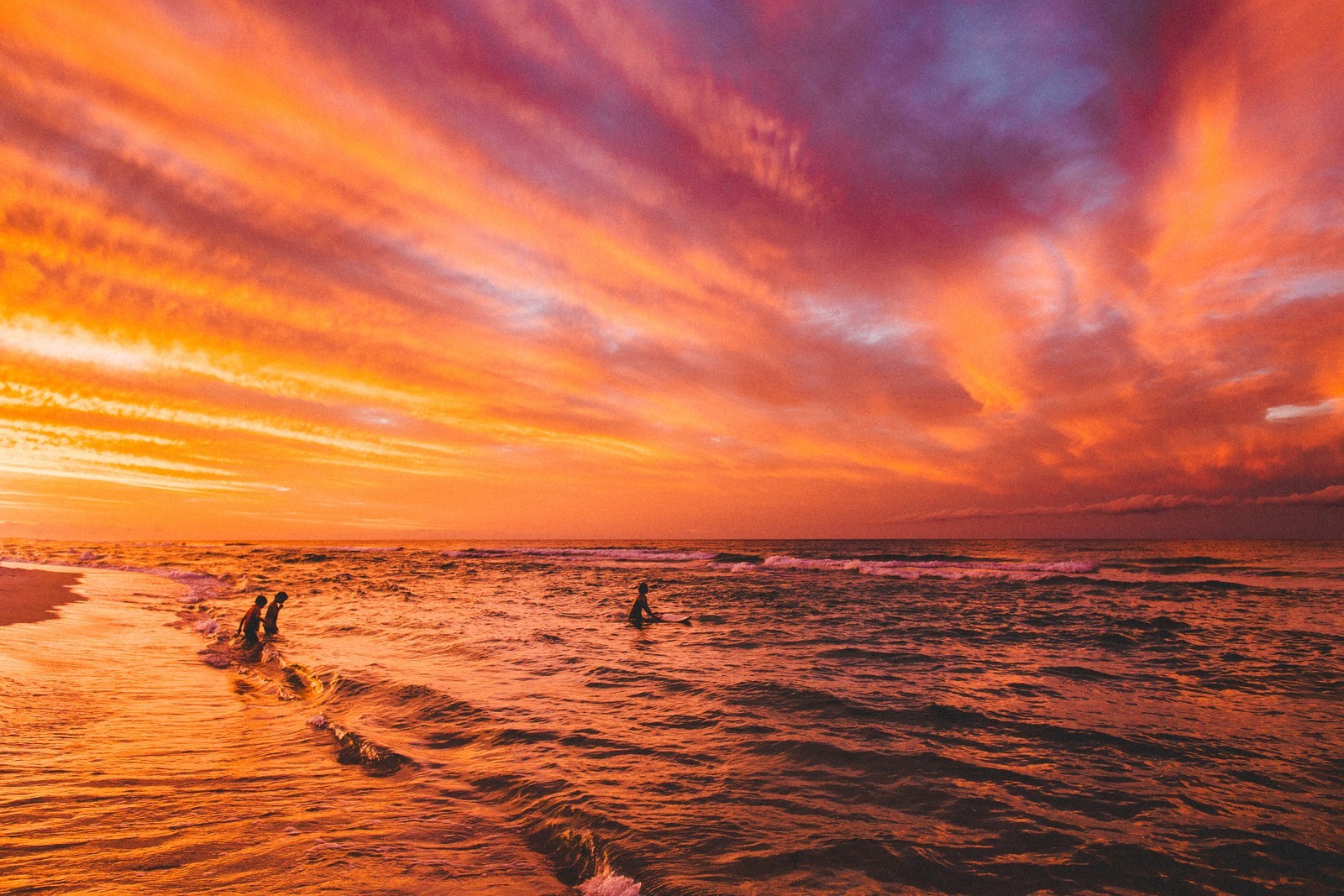 Sunset over the ocean with people in the water HD Wallpaper