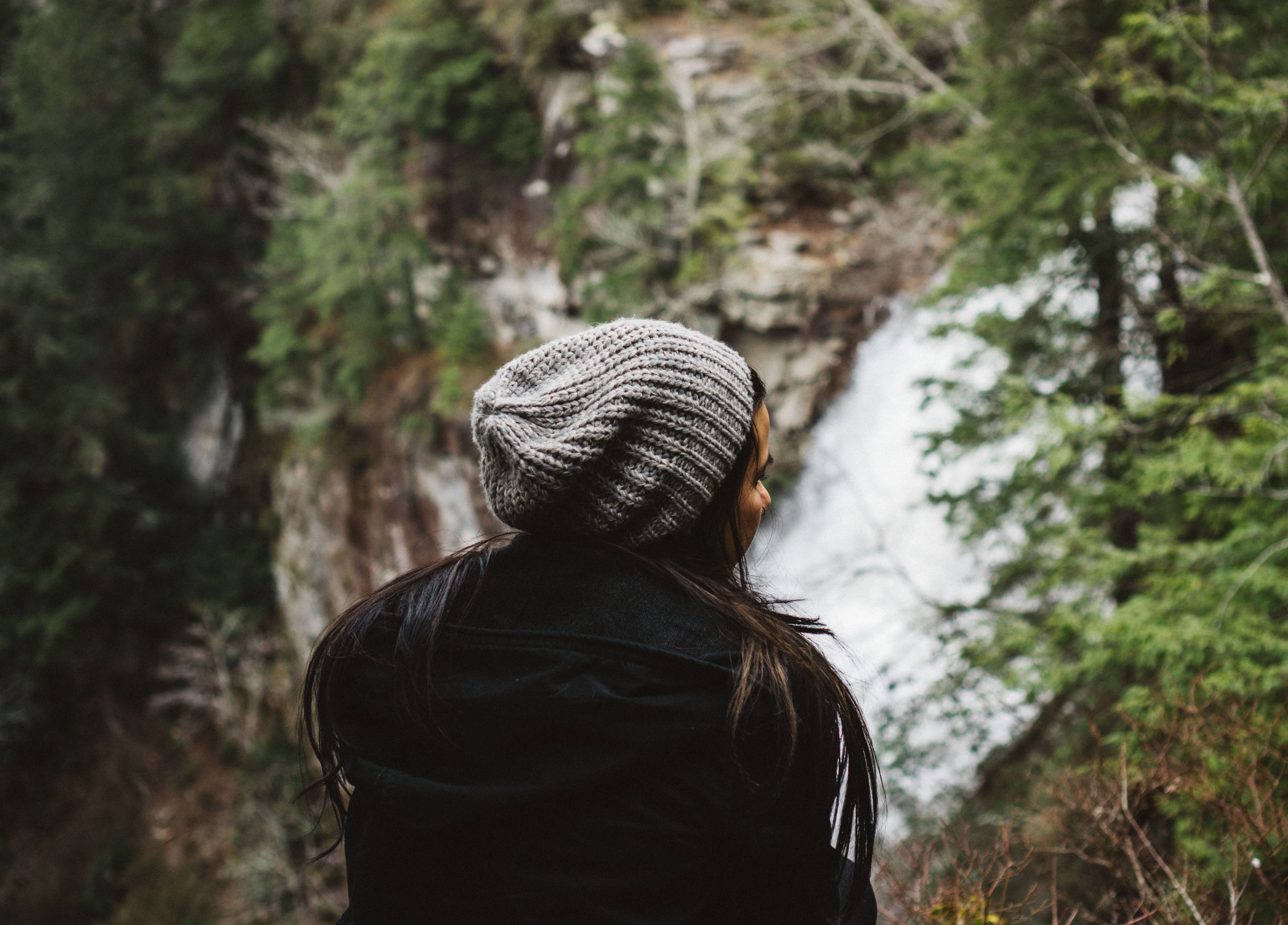 Woman in beanie looking at a waterfall HD Wallpaper