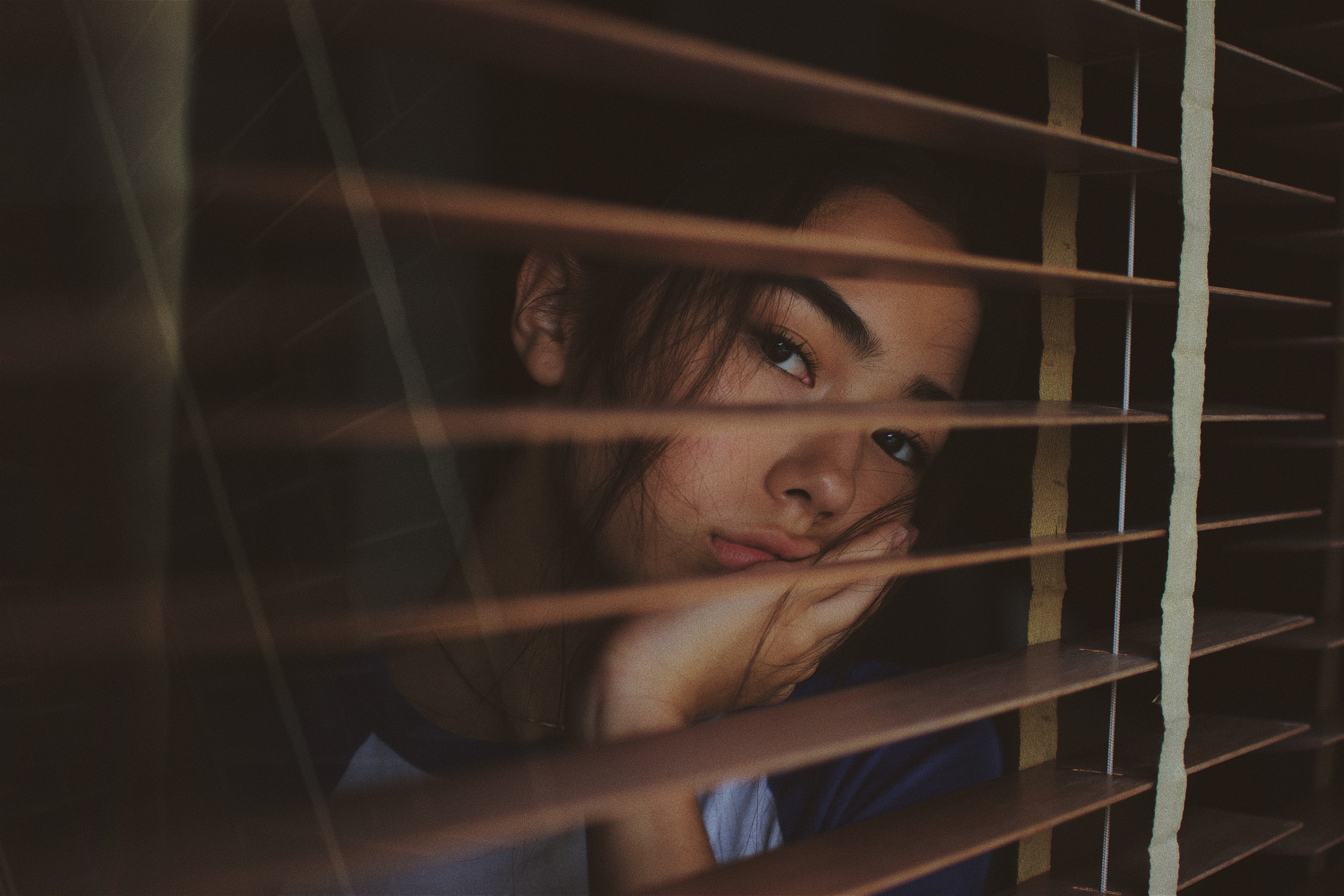 Woman resting her head on her hand behind blinds HD Wallpaper