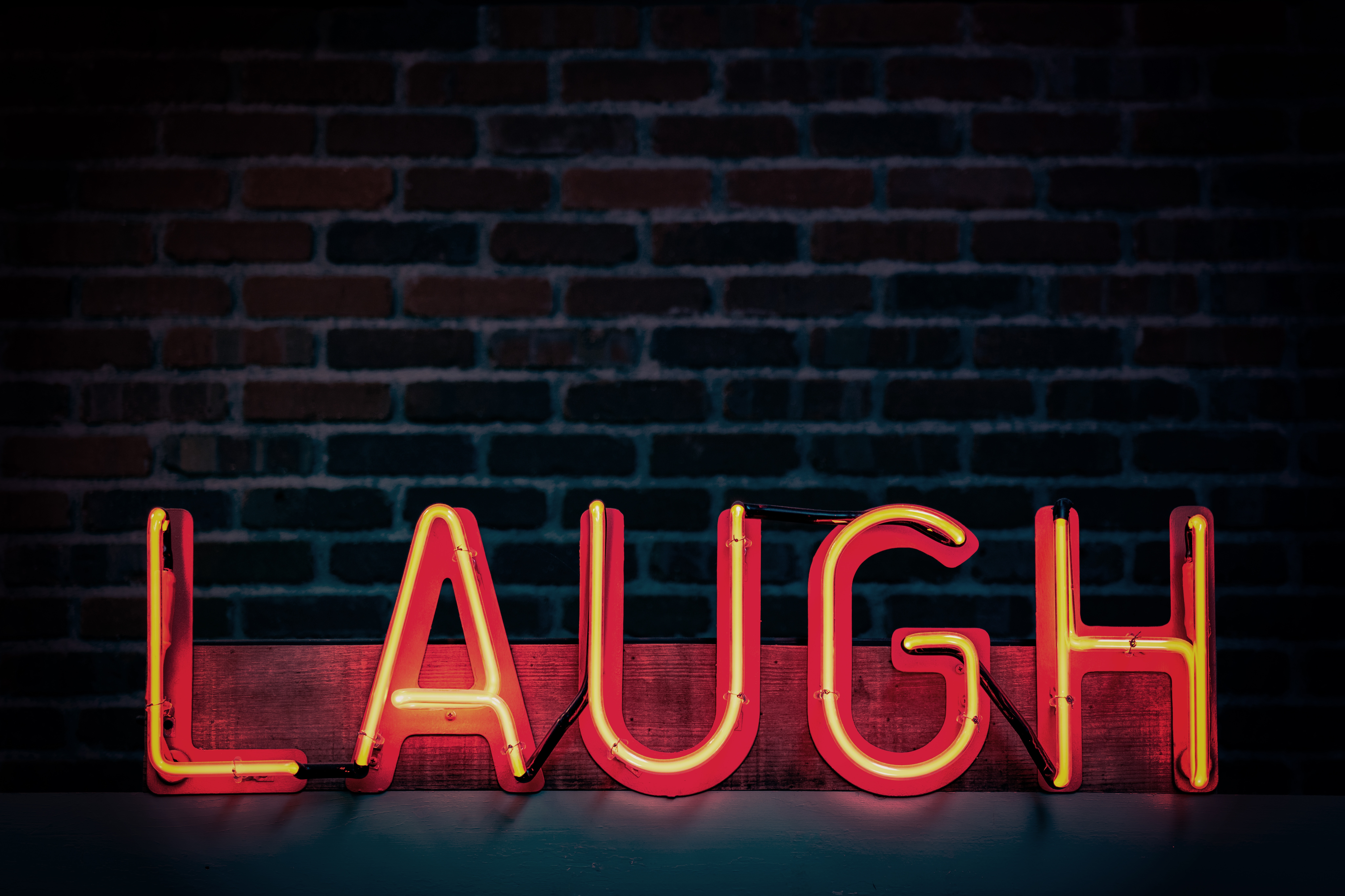 Neon sign spelling out LAUGH on a brick wall HD Wallpaper