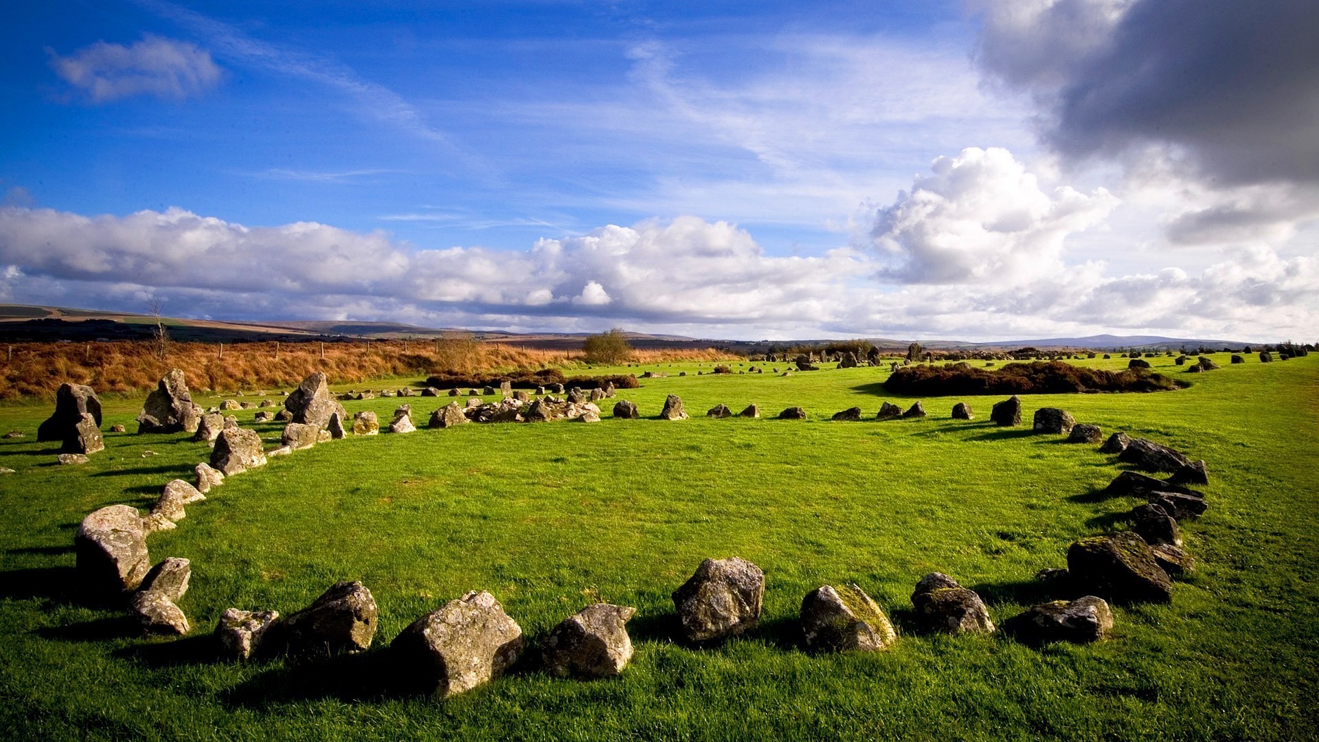 Ancient stone circle on a grassy field under a cloudy sky HD Wallpaper