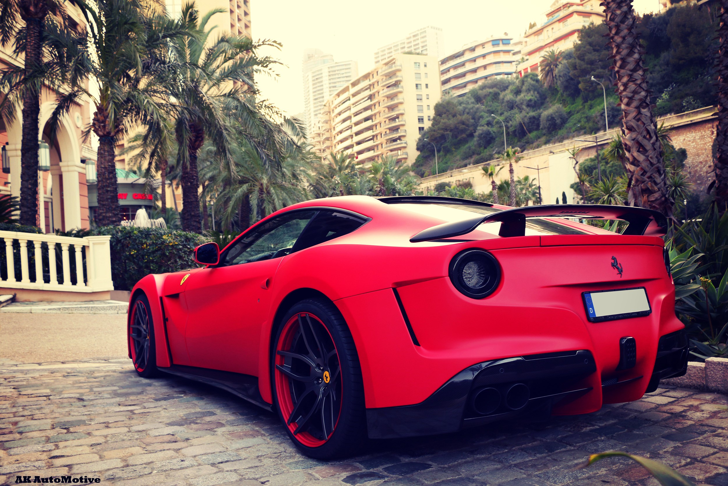 Red Ferrari F12berlinetta parked near palm trees and buildings HD Wallpaper