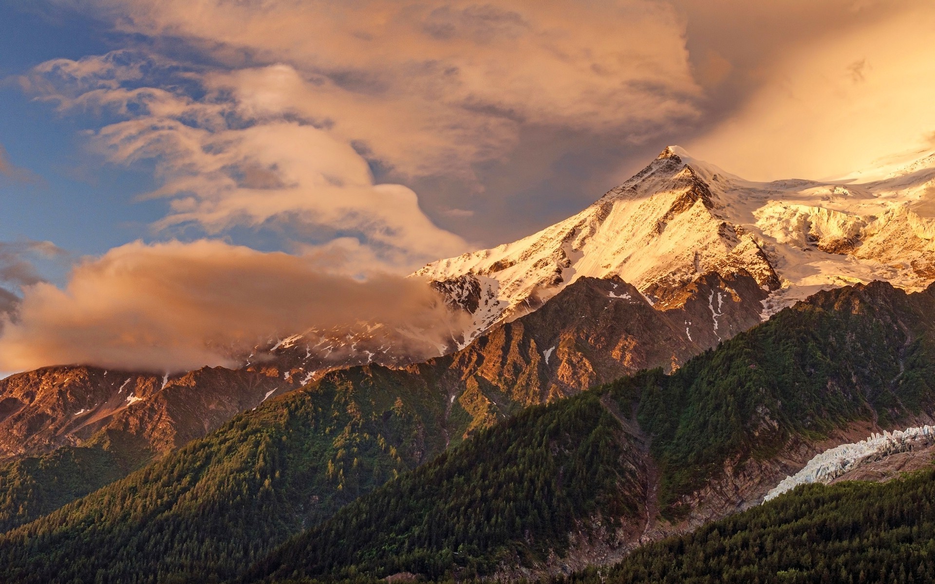 Snowy mountain peak at sunset with clouds and forest HD Wallpaper
