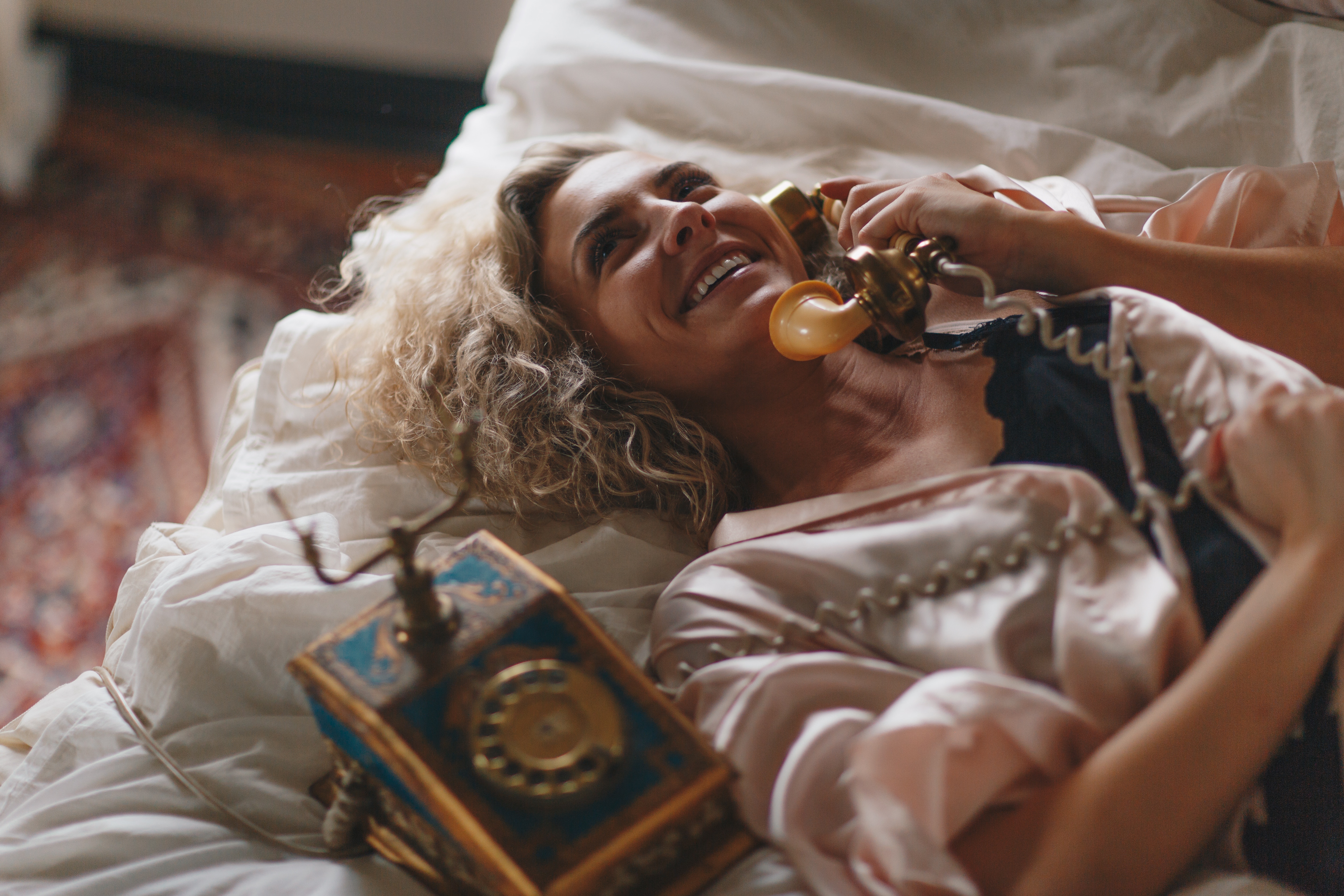 Woman with blonde curly hair on a bed with a vintage phone HD Wallpaper