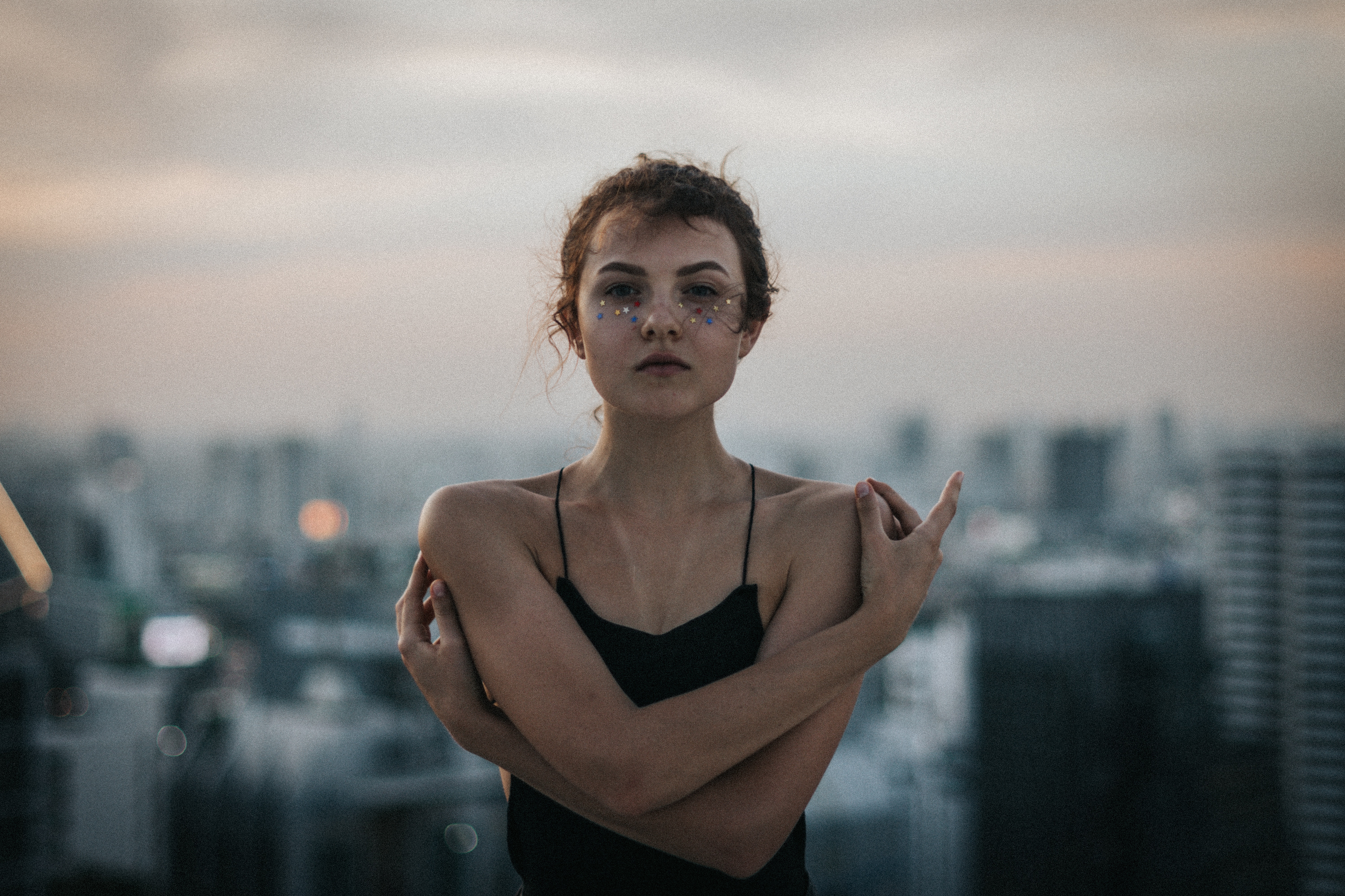 Woman with glitter makeup on a city rooftop at dusk HD Wallpaper