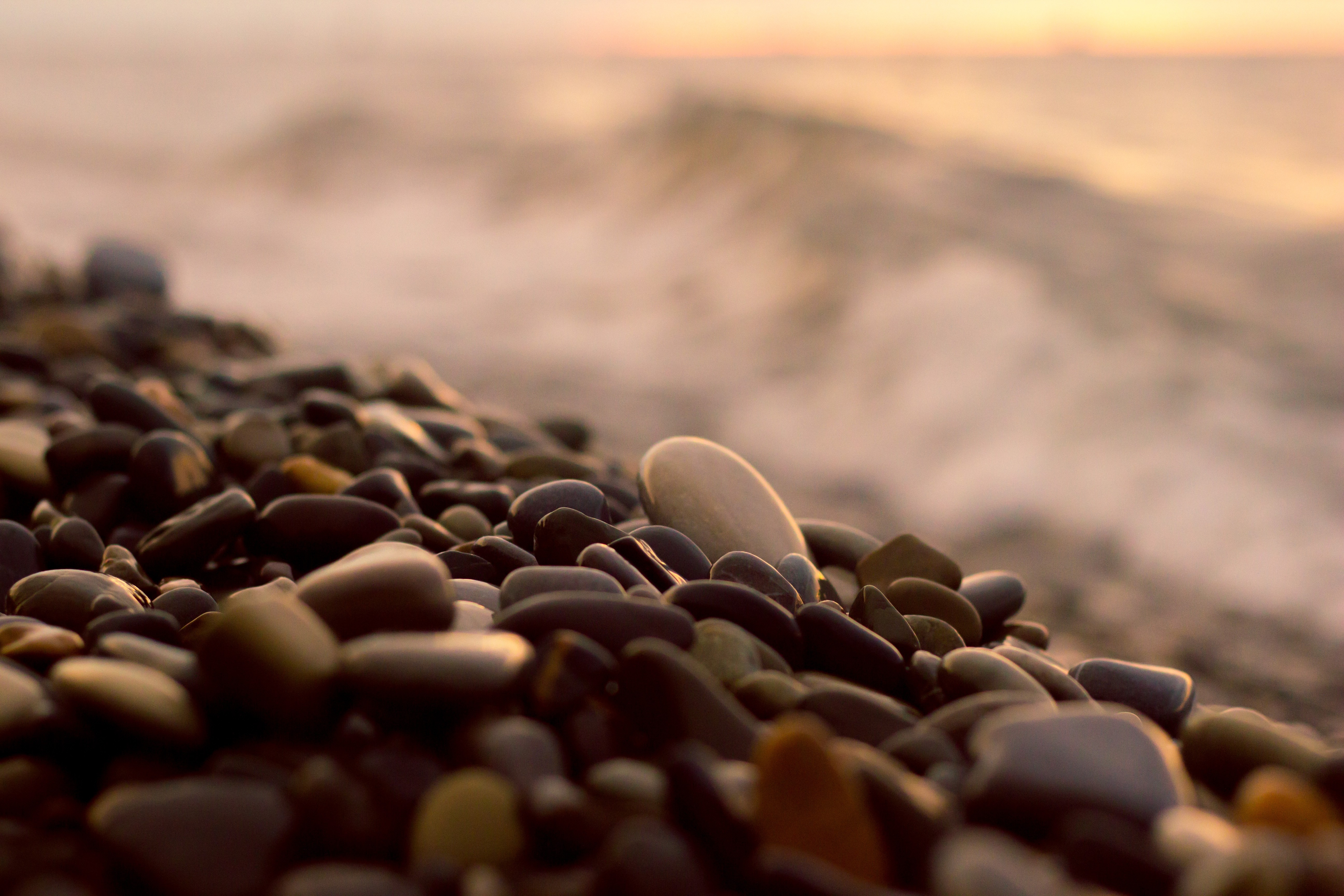 Pebbles on a beach with waves at sunset HD Wallpaper