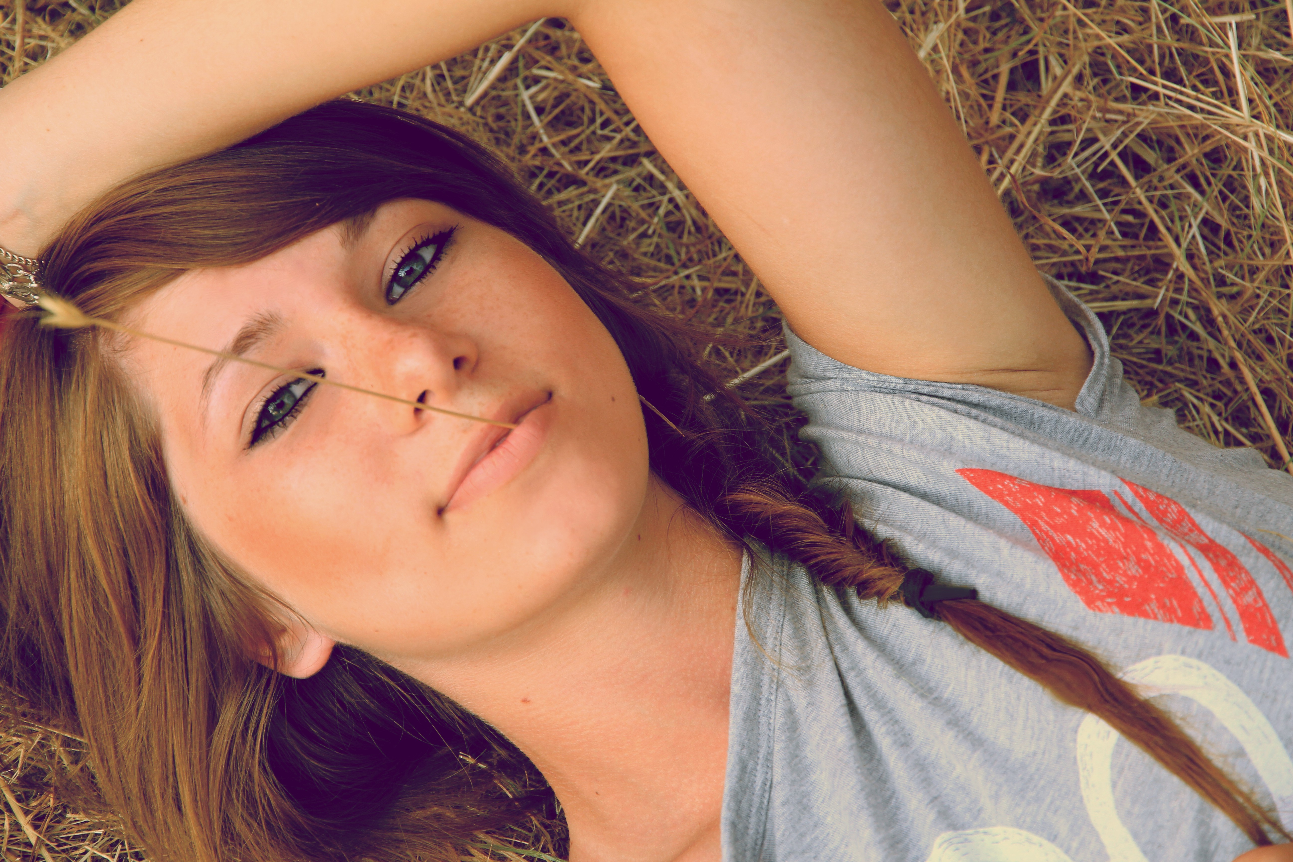 Woman with freckles lying in straw with a blade of grass HD Wallpaper