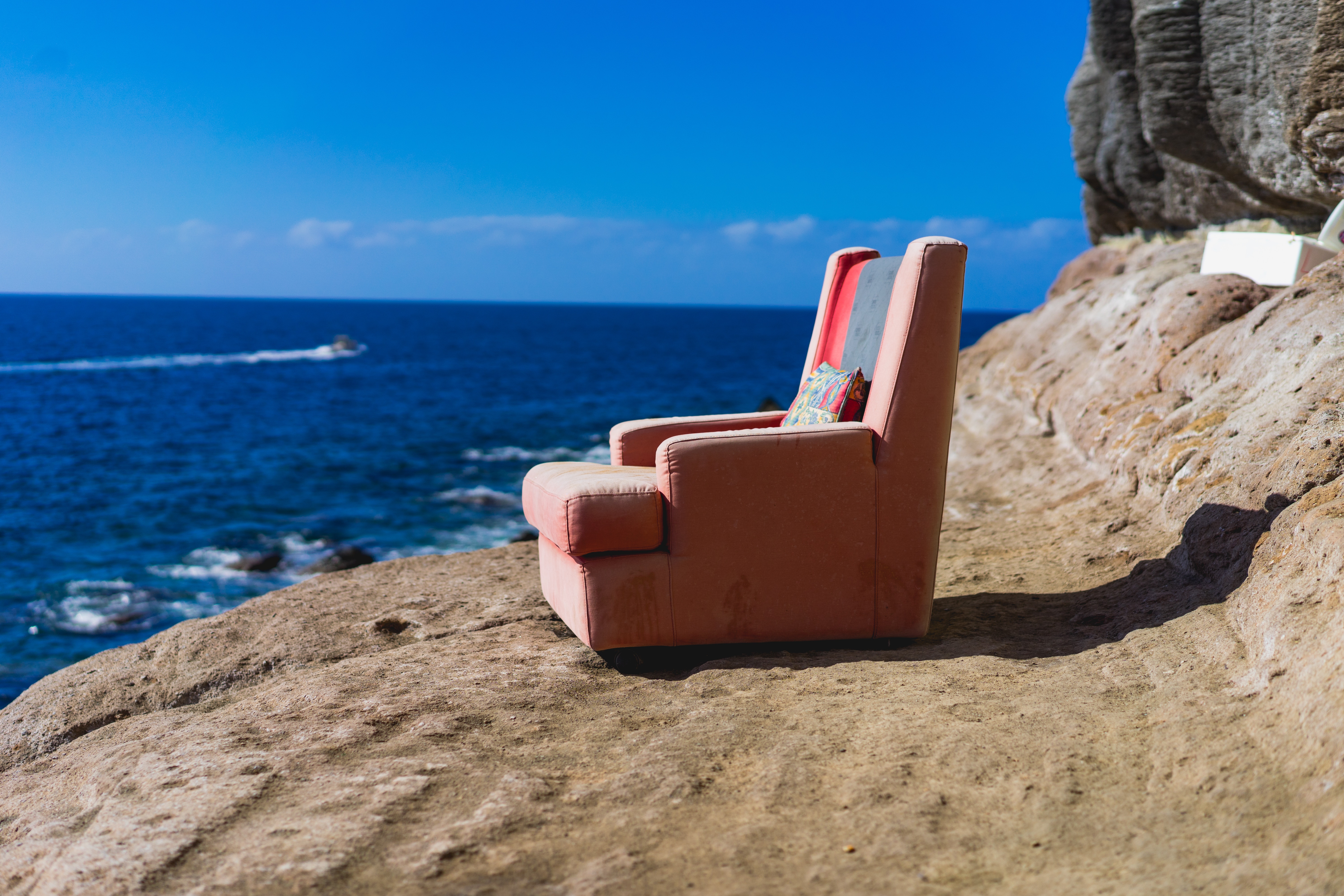 Pink armchair on a rocky coast overlooking the ocean HD Wallpaper
