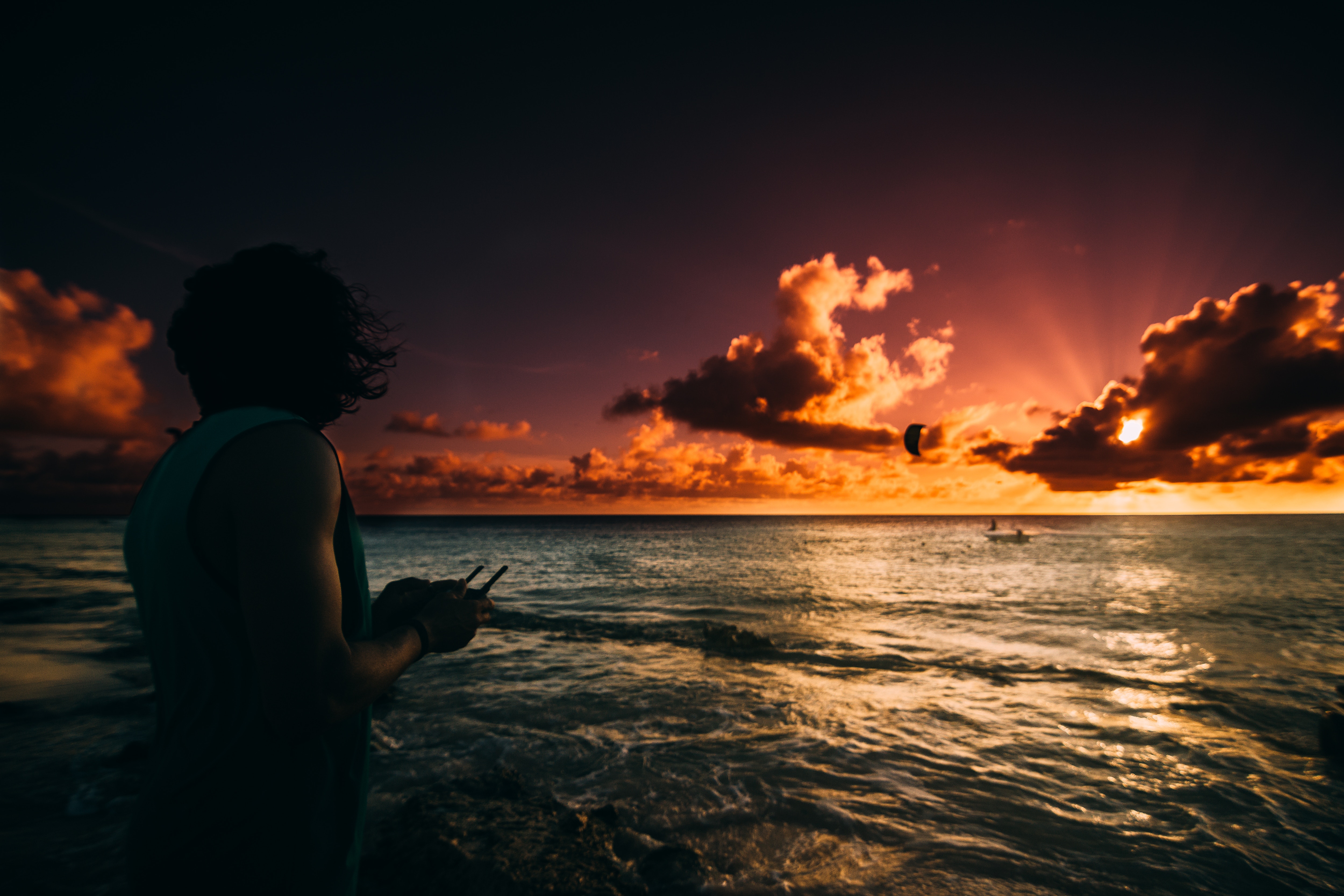 Person holding drone controller at sunset on beach HD Wallpaper